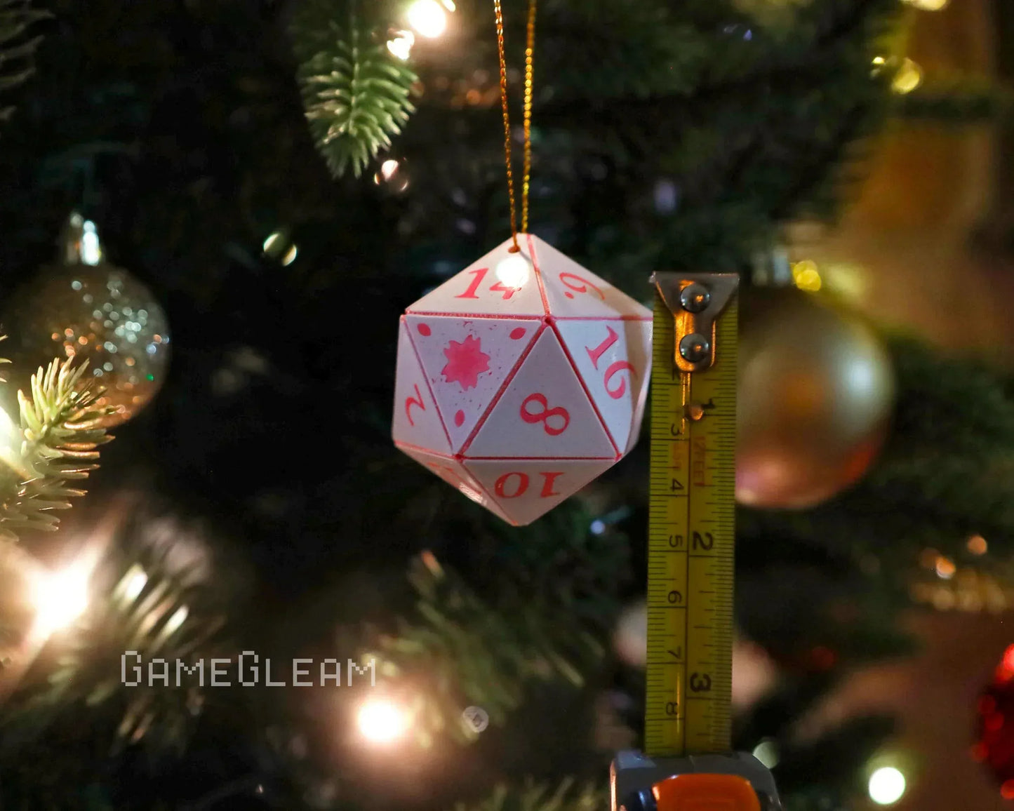 Large white 20-sided dice ornament with red numbers hanging on a Christmas tree, next to a tape measure.
