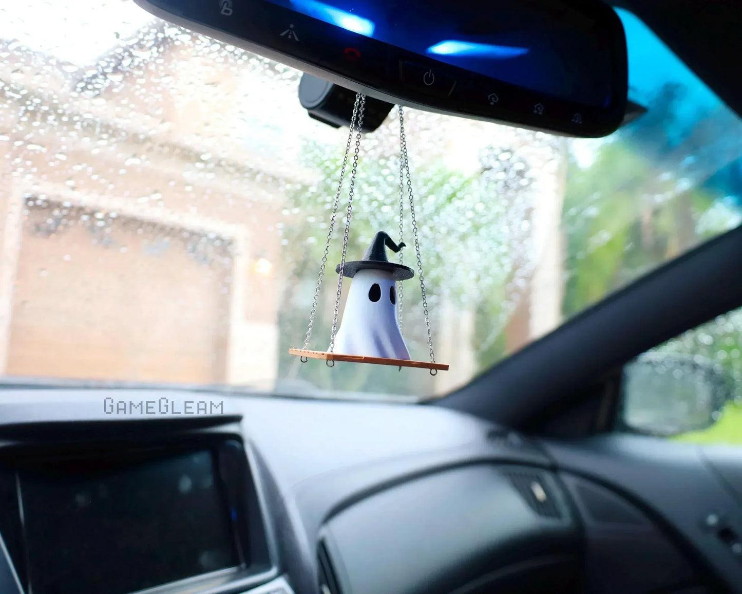 Handmade ghost charm with witch hat hanging from car mirror, indoor rainy day view