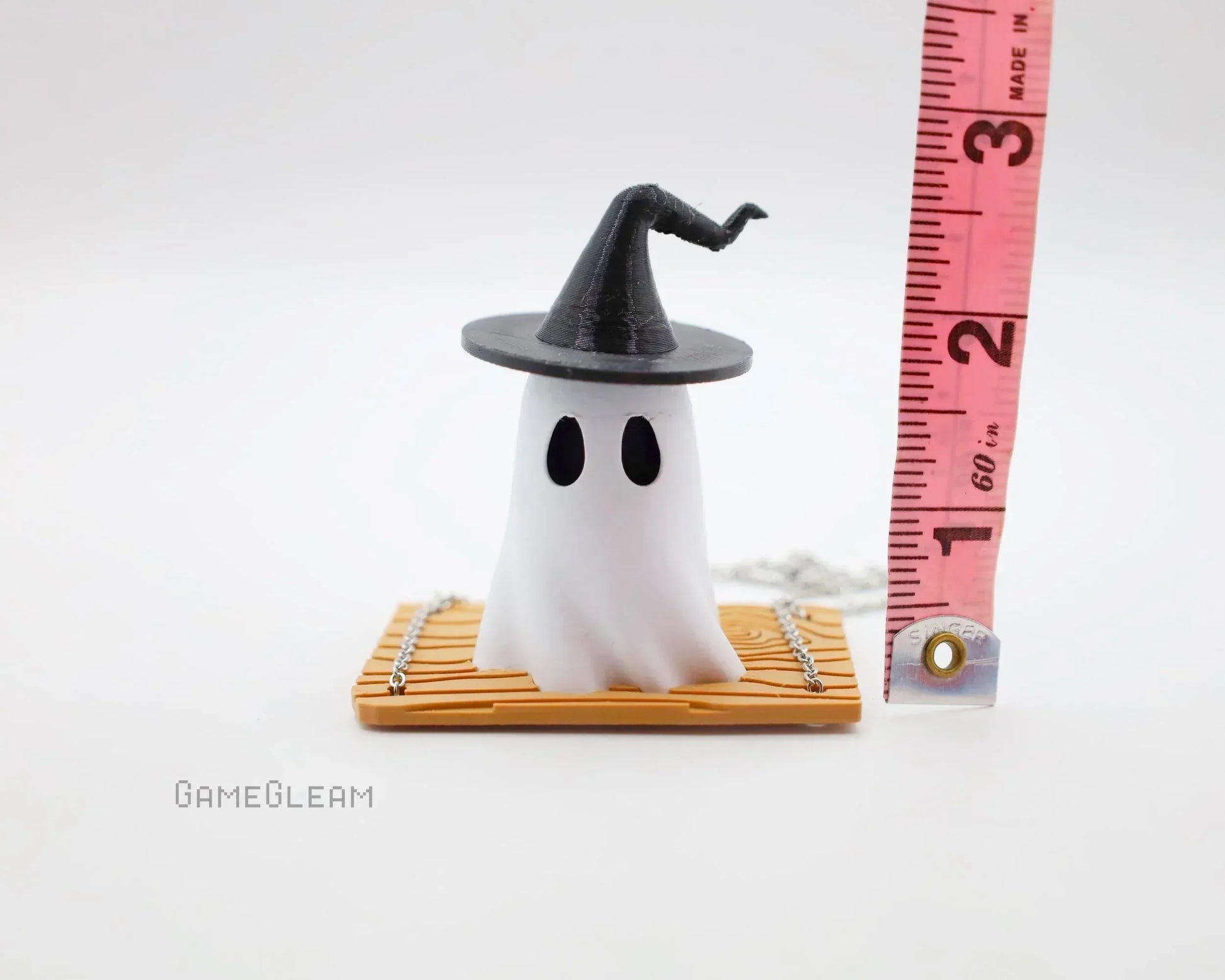 Handmade ghost figurine with wizard hat on miniature bamboo mat, measured with tape