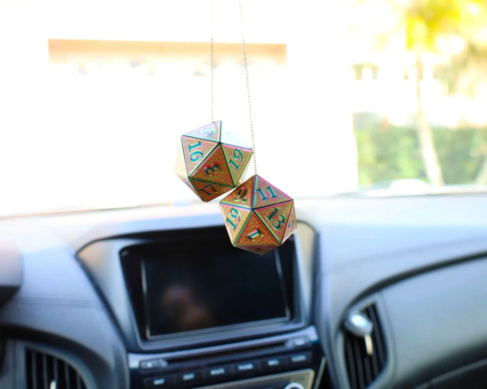 Holographic twenty-sided dice car accessory hanging from rearview mirror in modern vehicle interior.