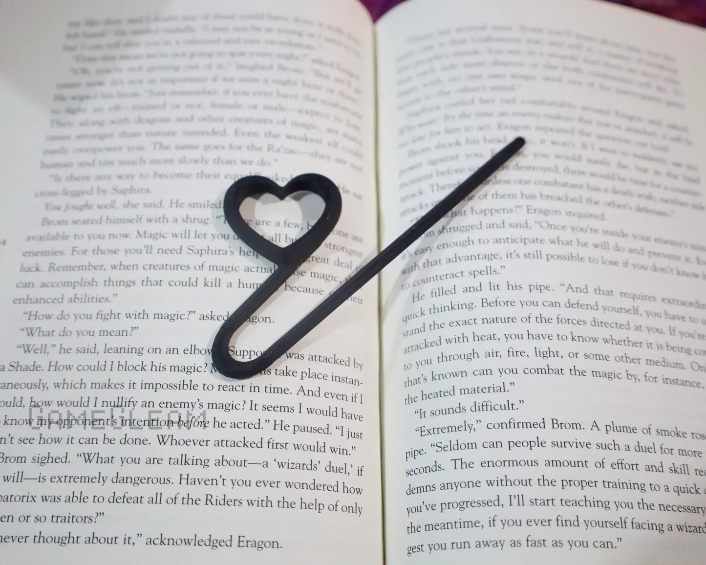 Heart-shaped black metal bookmark resting on an open fantasy novel