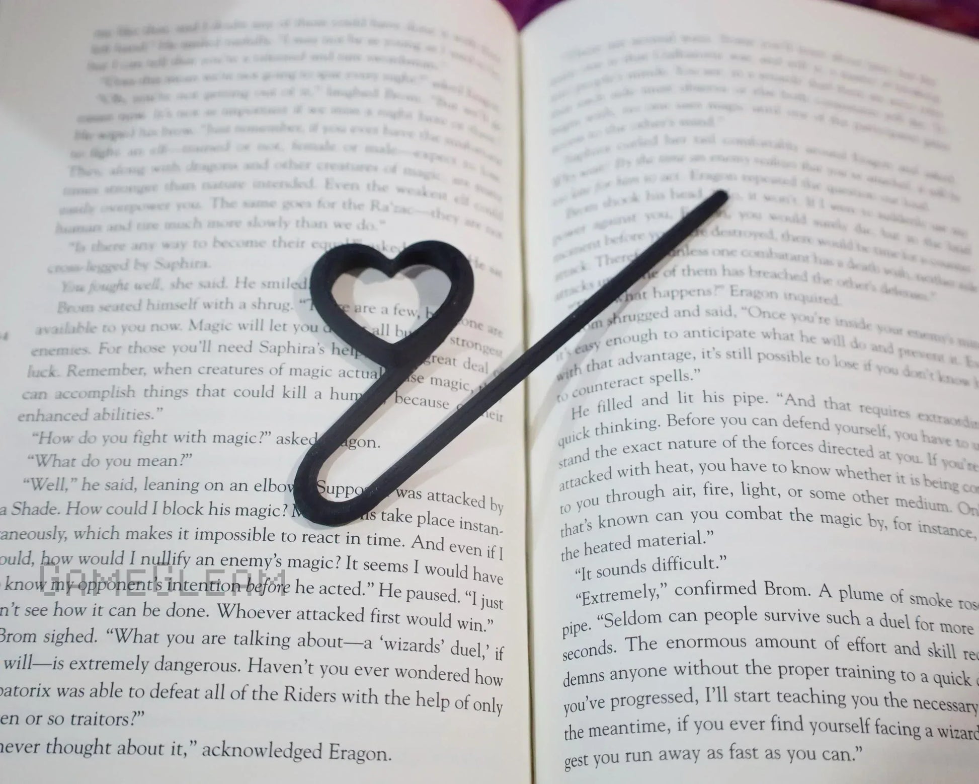 Heart-shaped black metal bookmark resting on an open fantasy novel