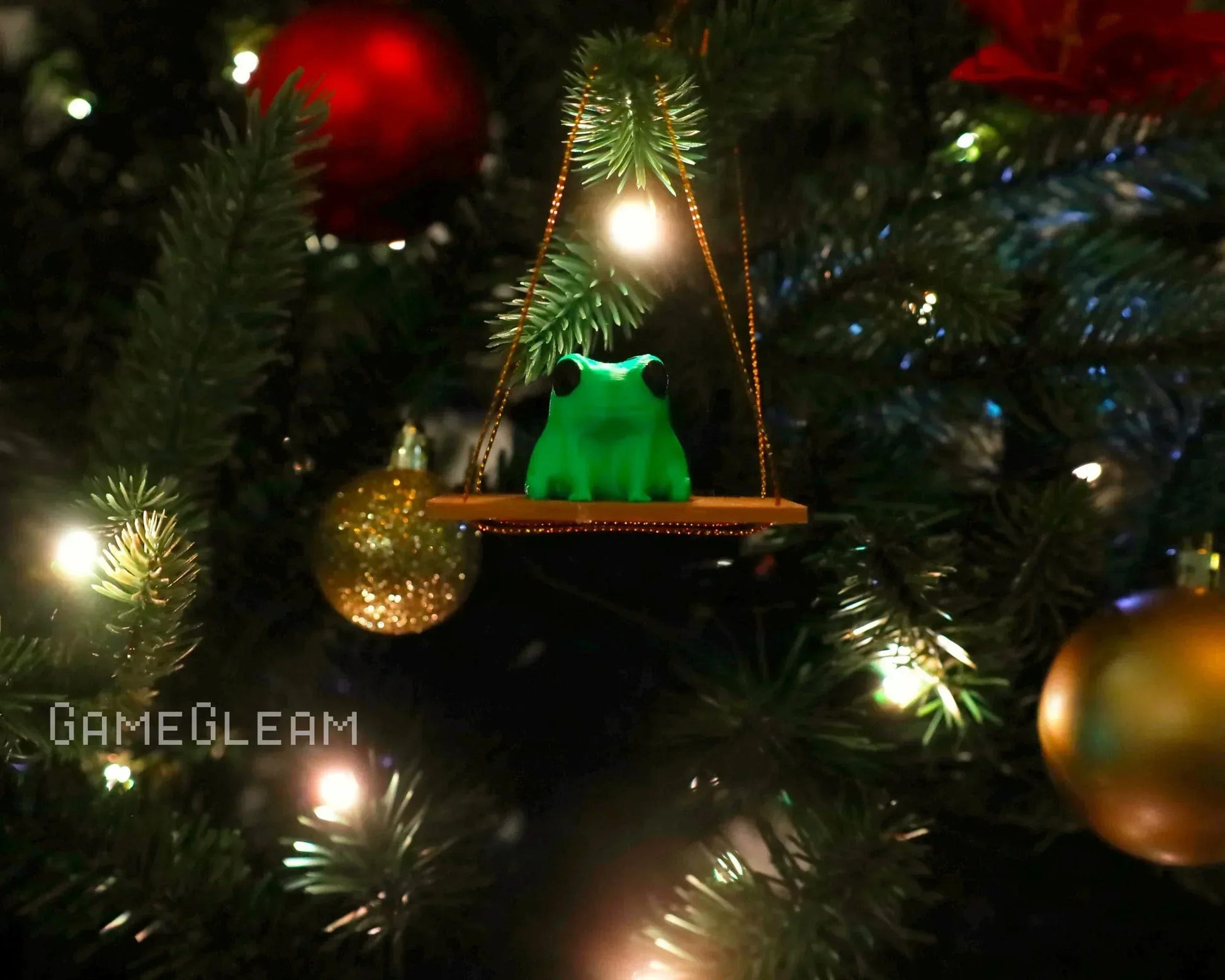 Green frog ornament on swing, hanging on a decorated Christmas tree with gold and red balls