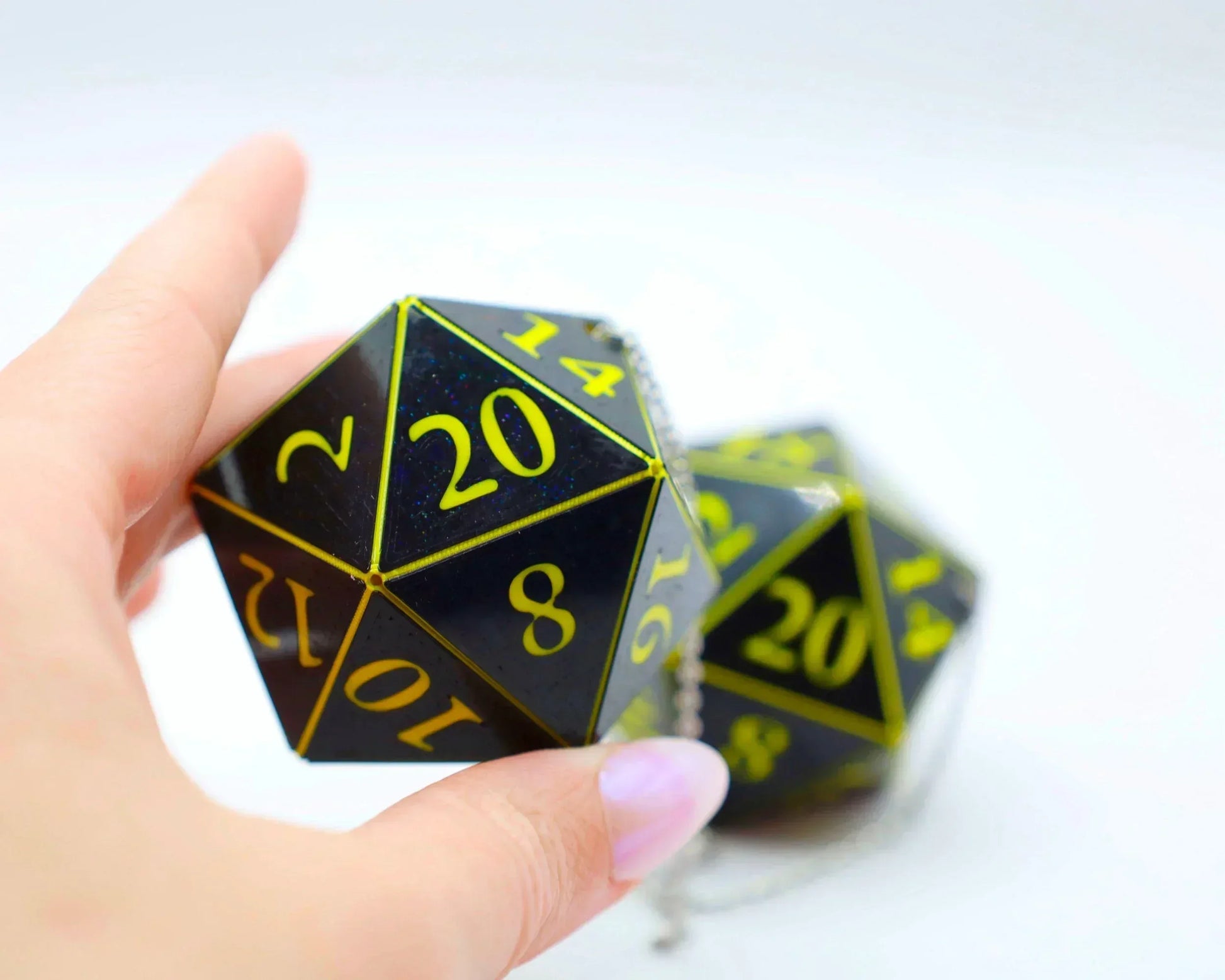 Hand holding black and yellow twenty-sided dice car charm with chain for tabletop gamers