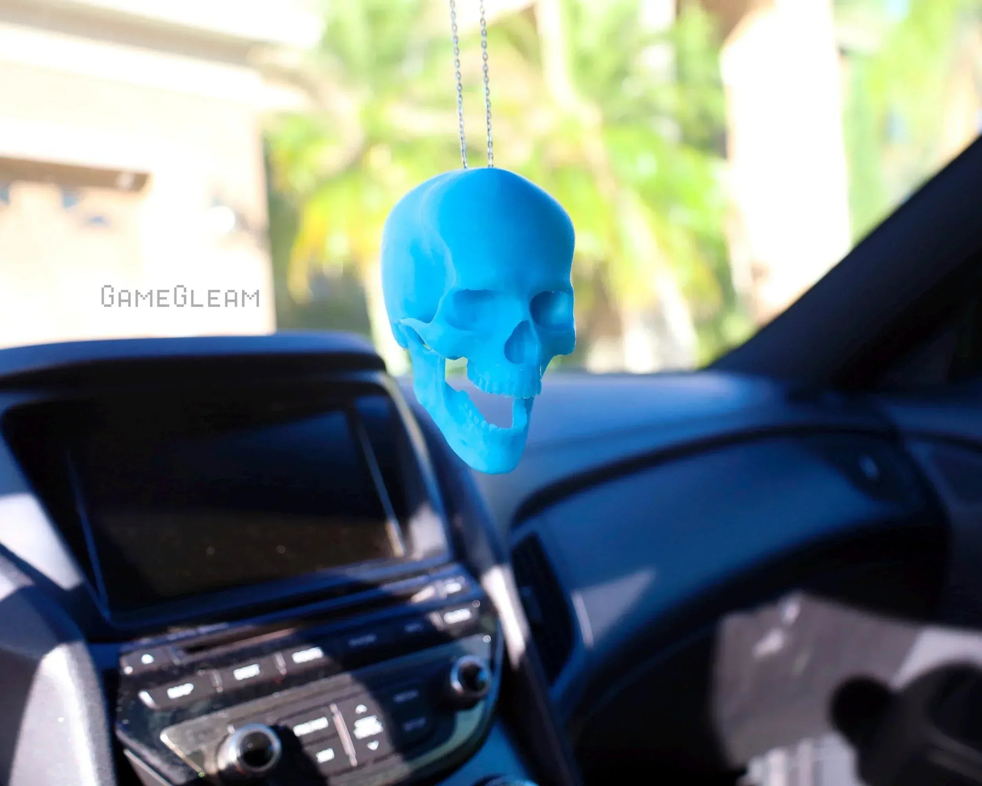 Blue skull-shaped car charm hanging from rearview mirror in a sunlit car interior