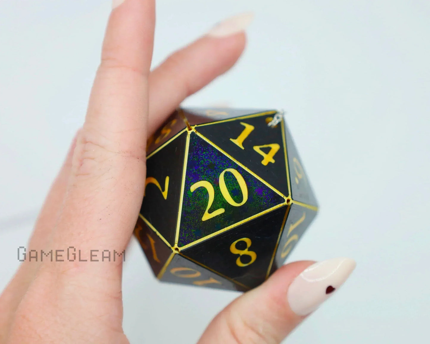 Hand holding a large holographic black 20-sided dice with gold numbers, gamer accessory