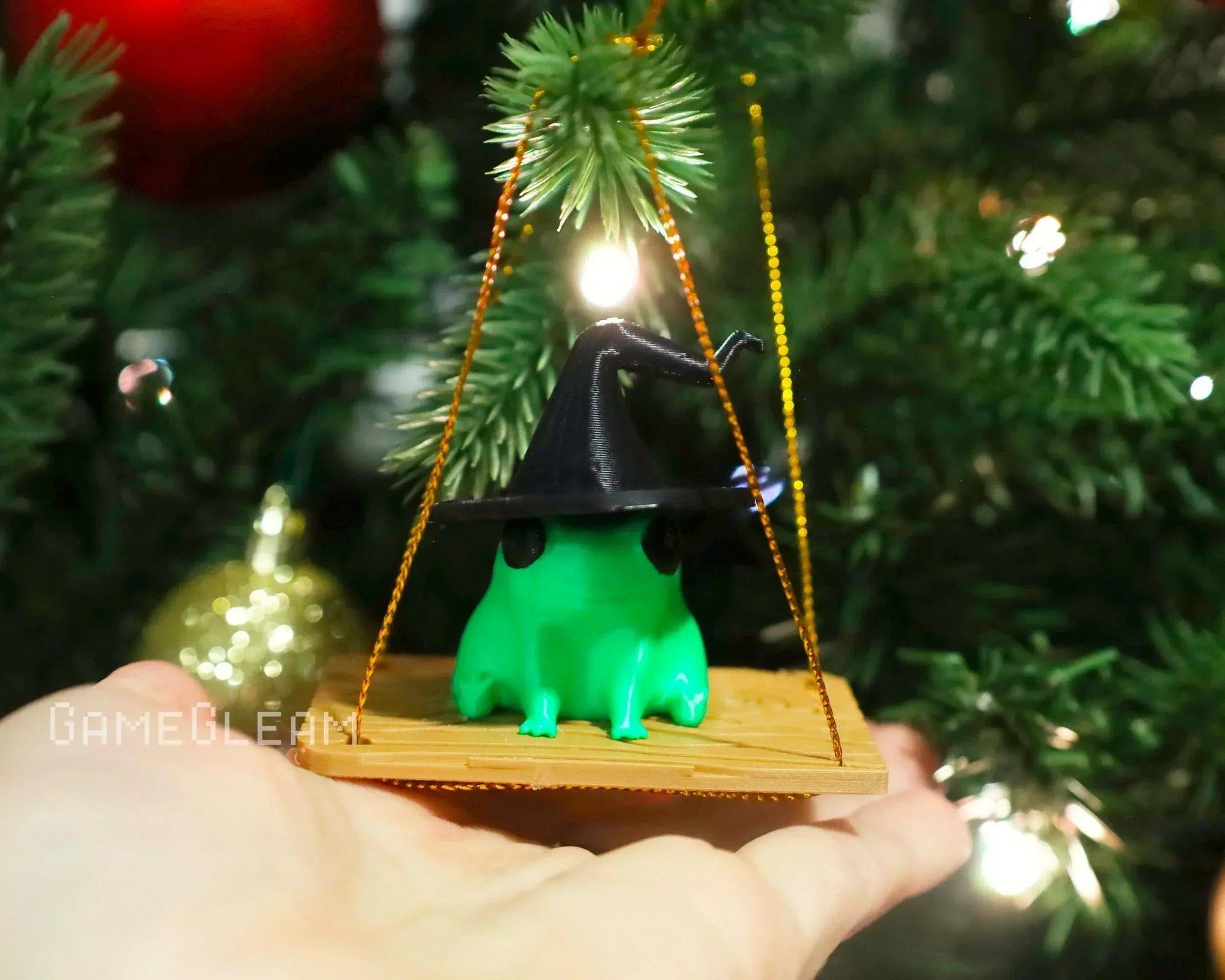 Green frog figurine with black wizard hat ornament hanging on a Christmas tree branch