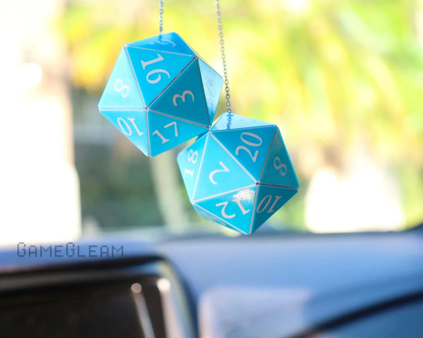 Blue 20-sided dice car charm hanging from rearview mirror with sunlight background