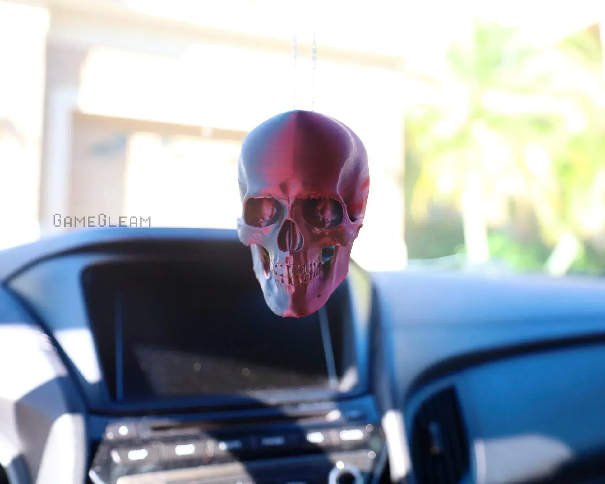 Holographic pink skull car charm hanging from rearview mirror in vehicle interior