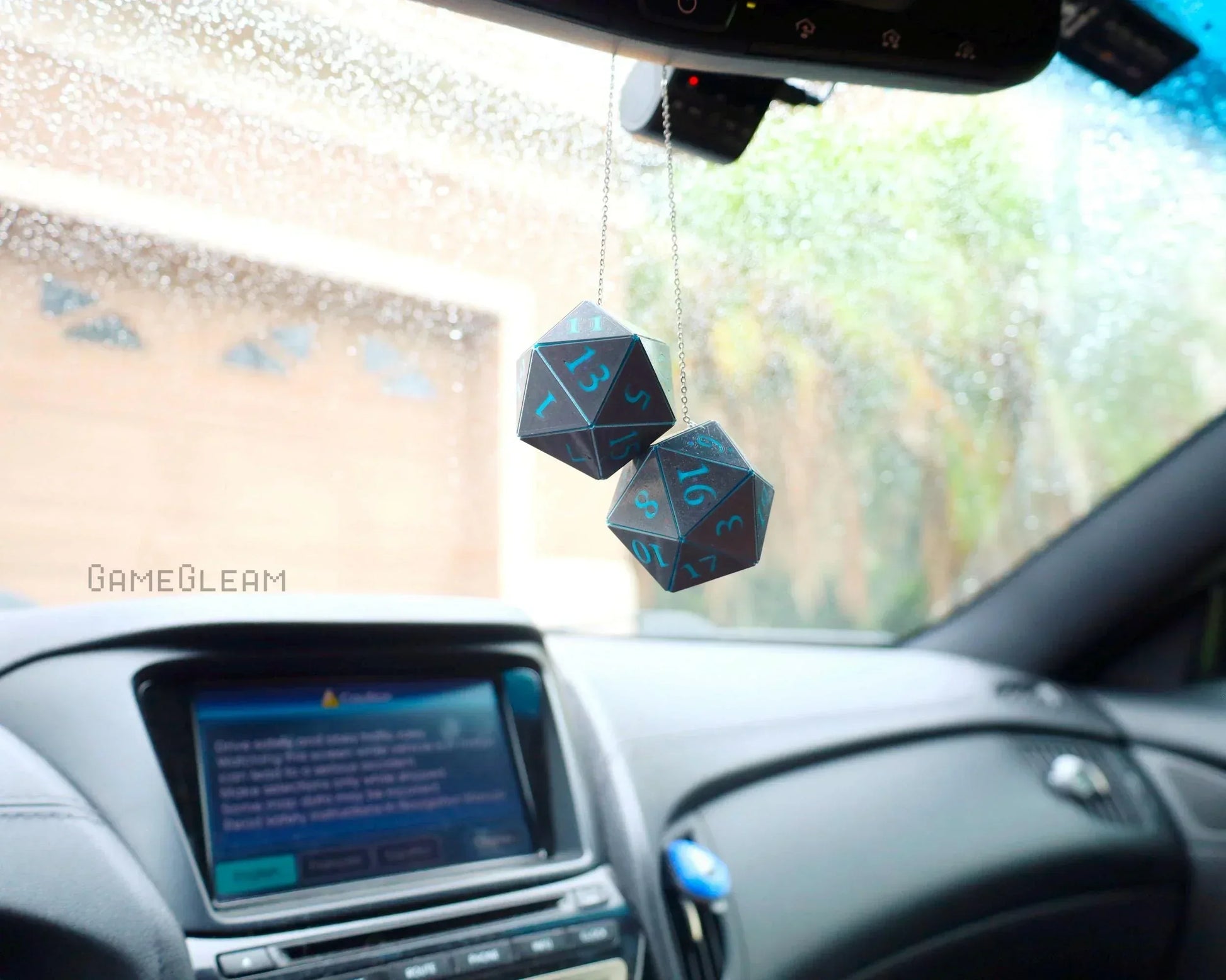 Holographic polyhedral dice car charm hanging from rearview mirror in a modern car interior.