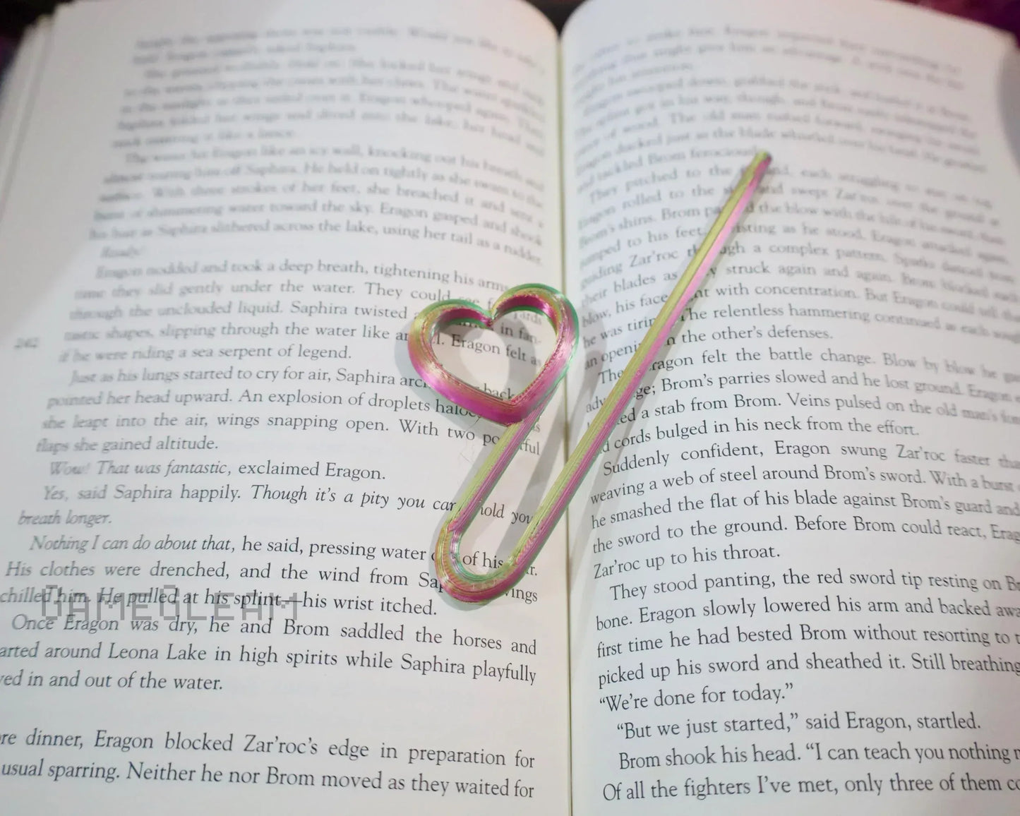 Heart-shaped rainbow metal bookmark resting on an open fantasy novel
