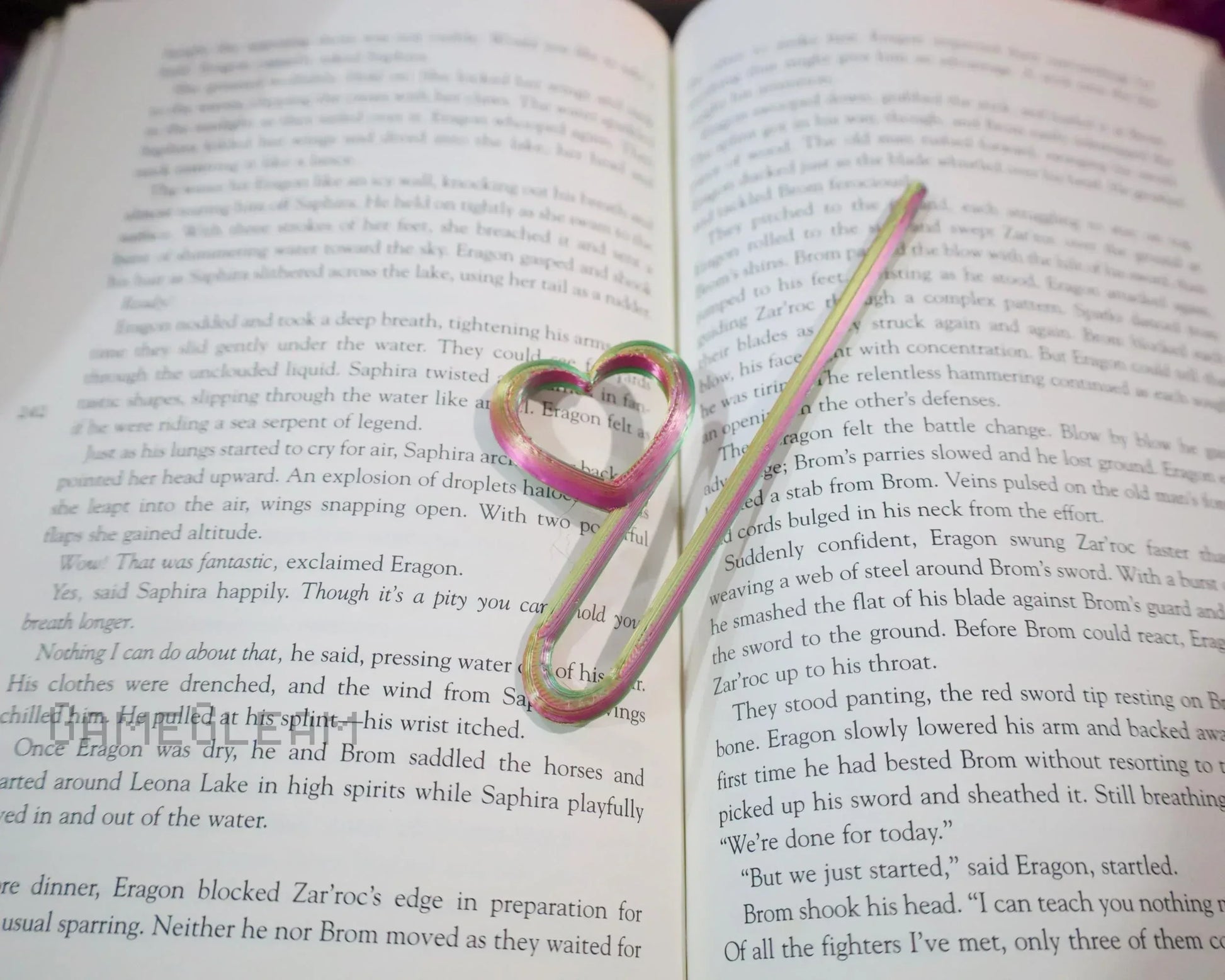 Heart-shaped rainbow metal bookmark resting on an open fantasy novel