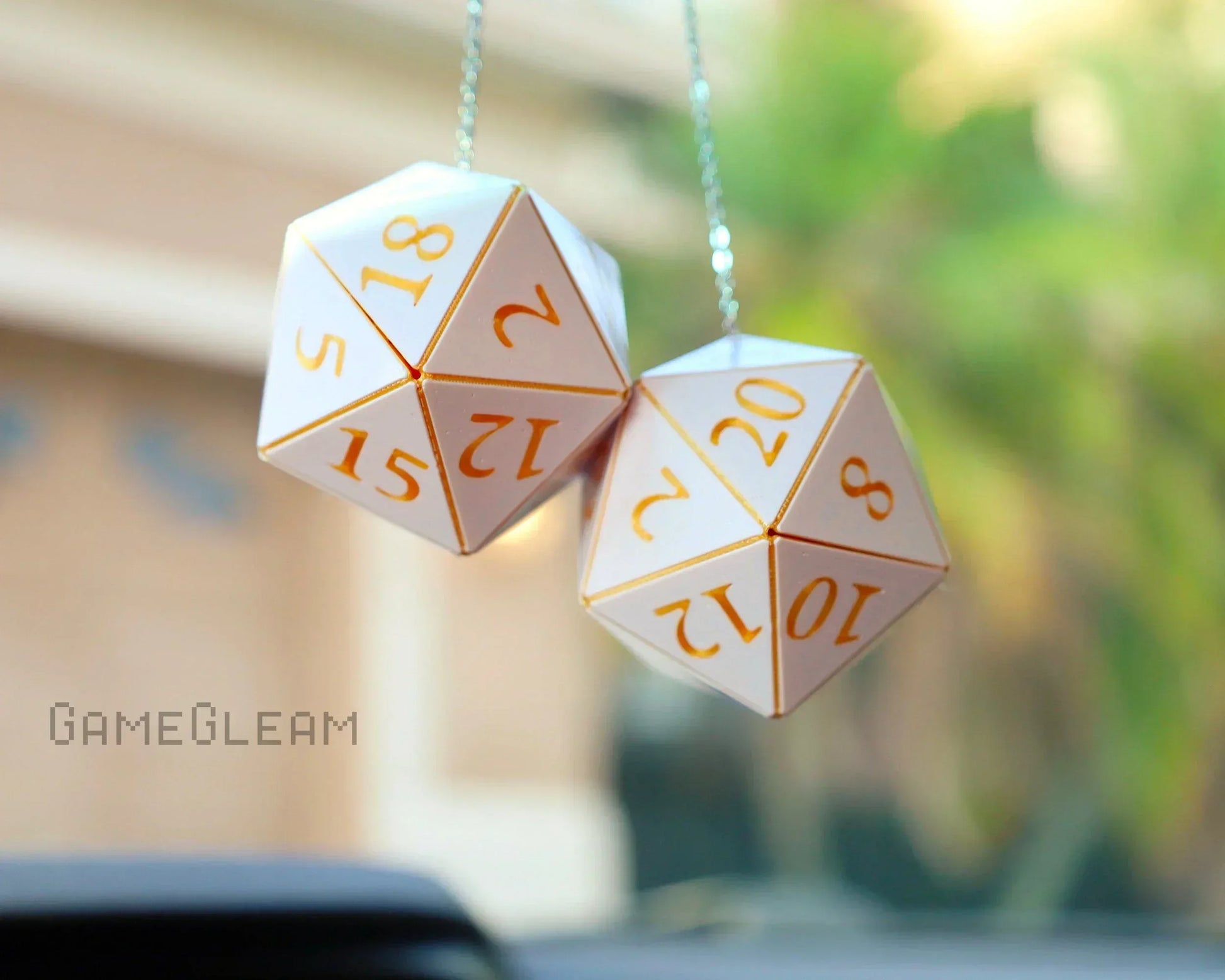 White twenty-sided dice car charms with gold numbers hanging from a rearview mirror