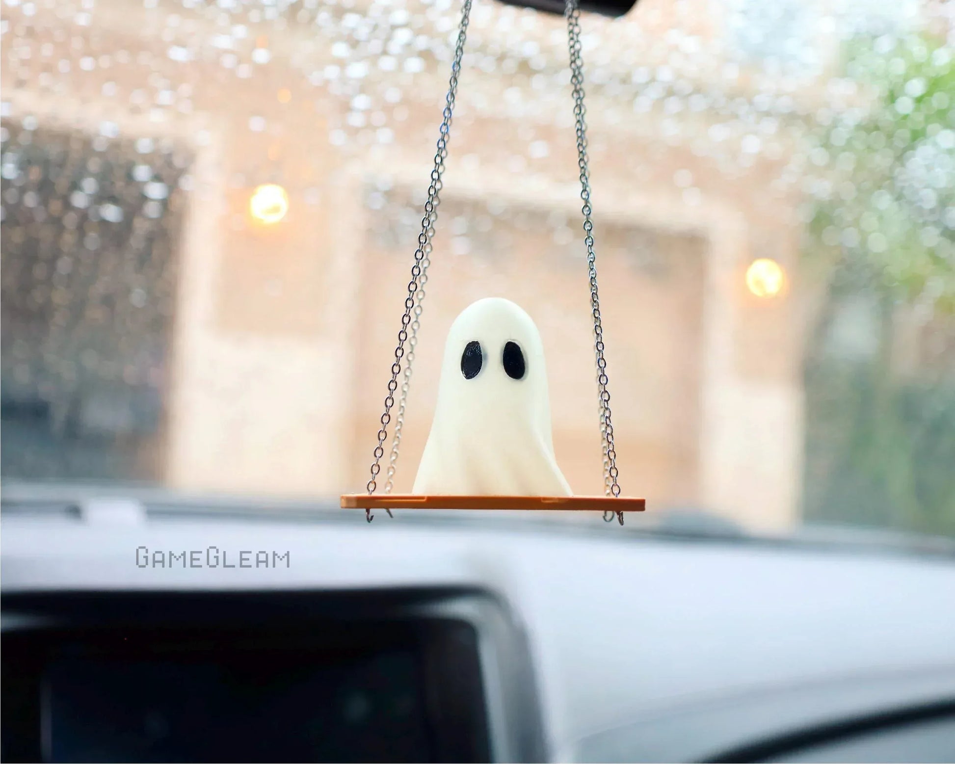 Handmade ghost car charm on swing with chain, hanging from rearview mirror, rainy window view