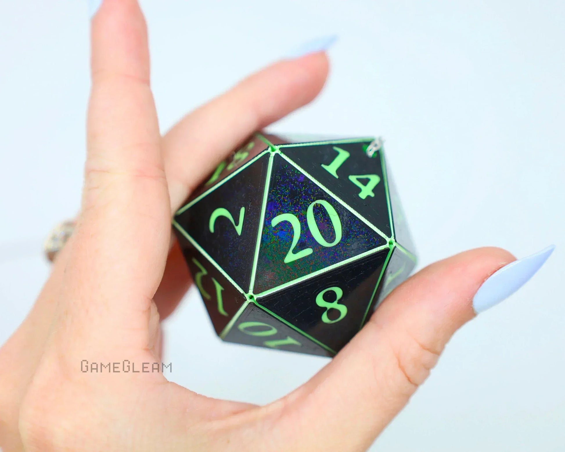 Hand holding a large black holographic 20-sided gaming dice with green numbers