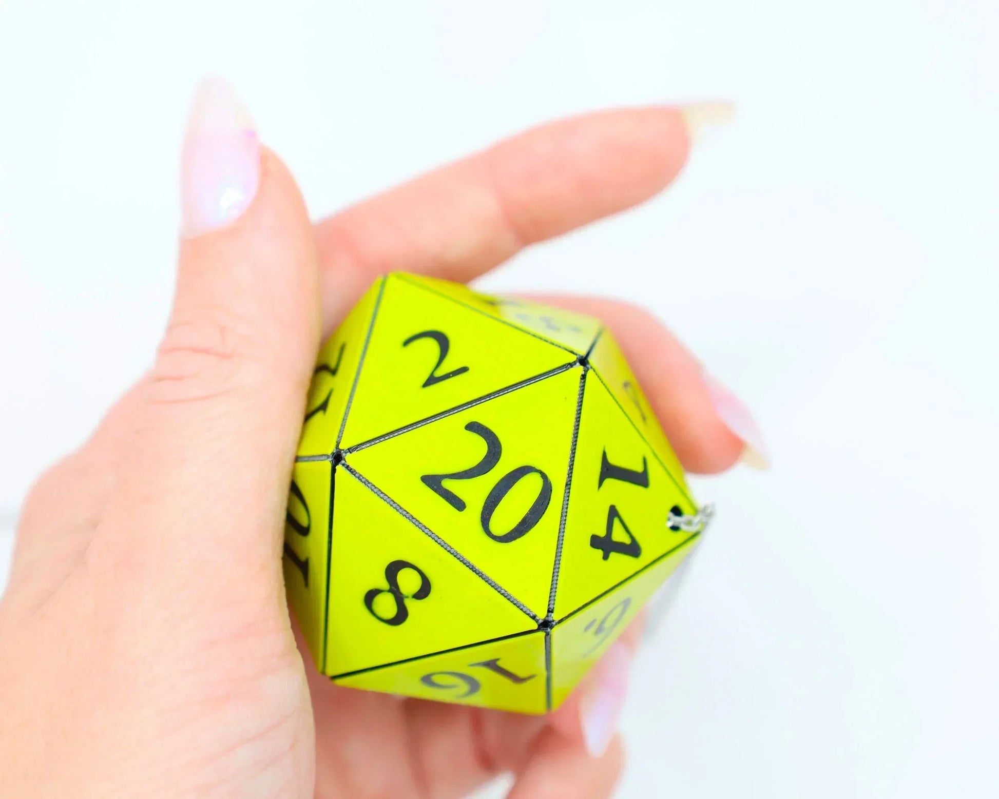 Hand holding a large yellow twenty-sided dice charm with black numbers for tabletop games