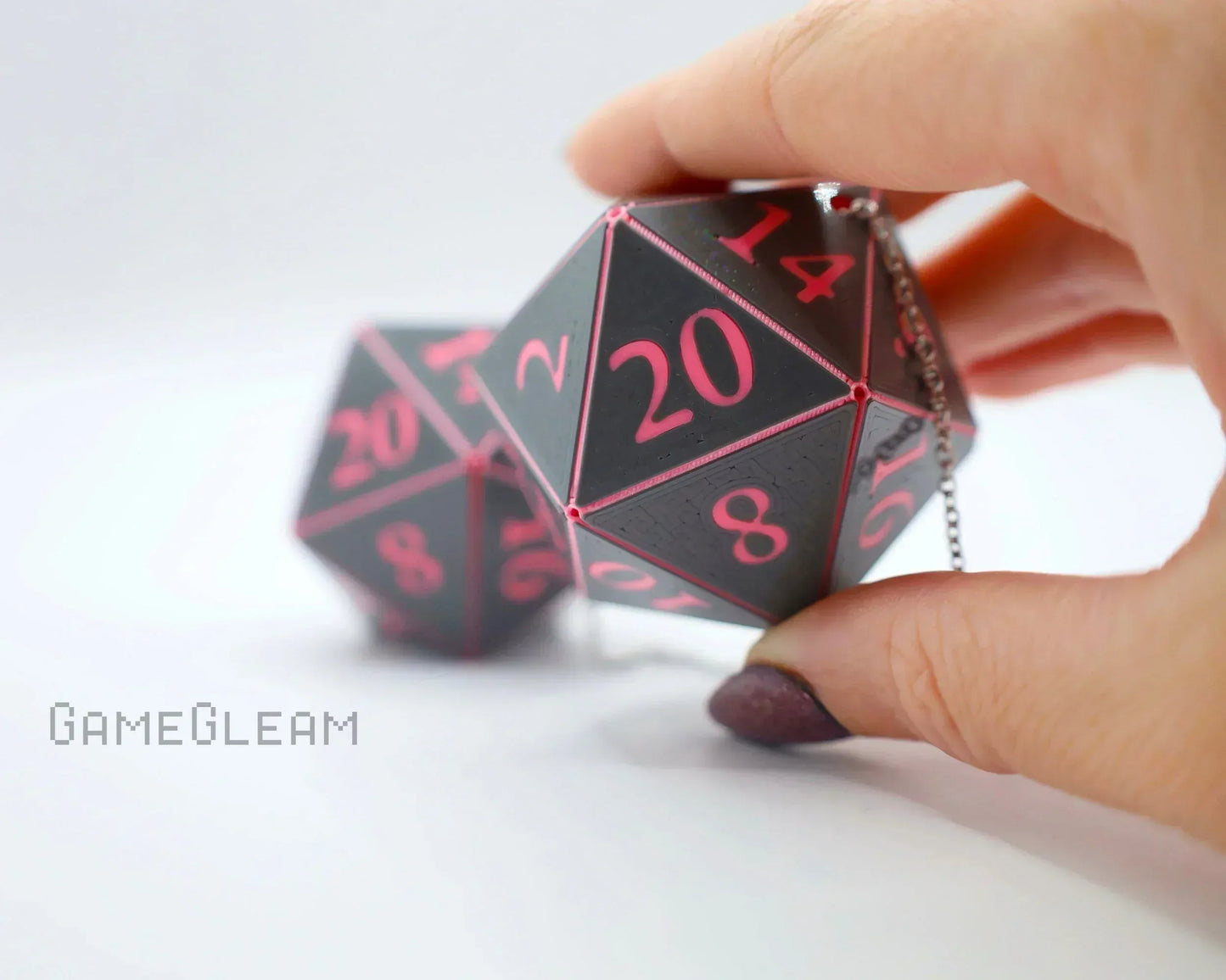 Hand holding a black and pink twenty-sided dice car charm with chain, for tabletop gamers.