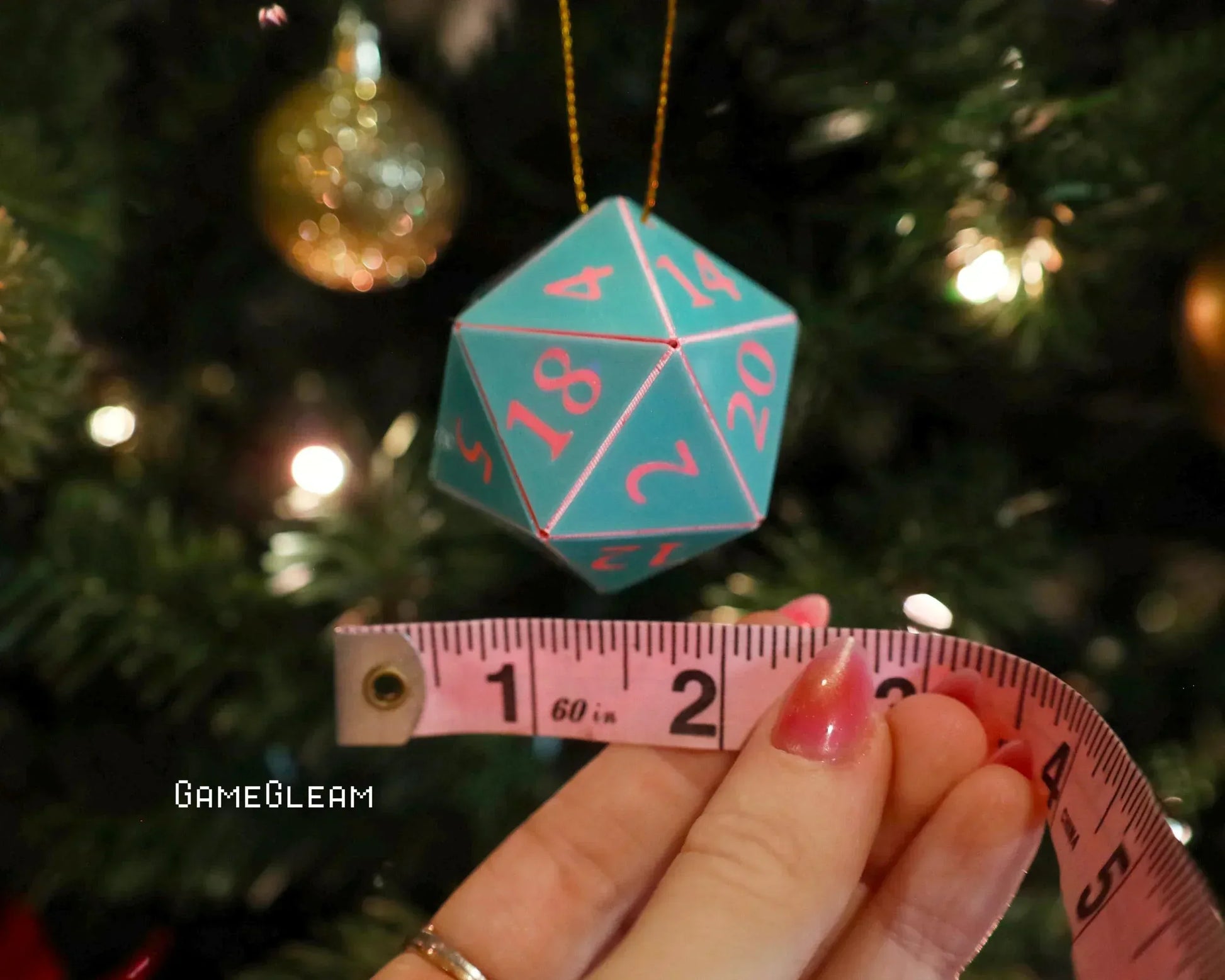Turquoise twenty-sided dice ornament measured with pink tape, hanging on a Christmas tree