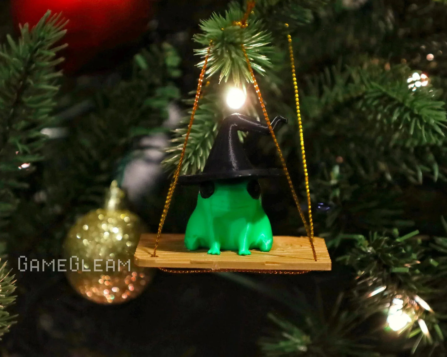 Green frog ornament with wizard hat on a swing hanging from a Christmas tree branch