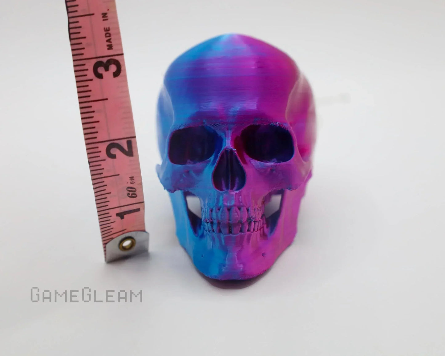 Small iridescent blue and purple skull decoration next to a measuring tape on white background