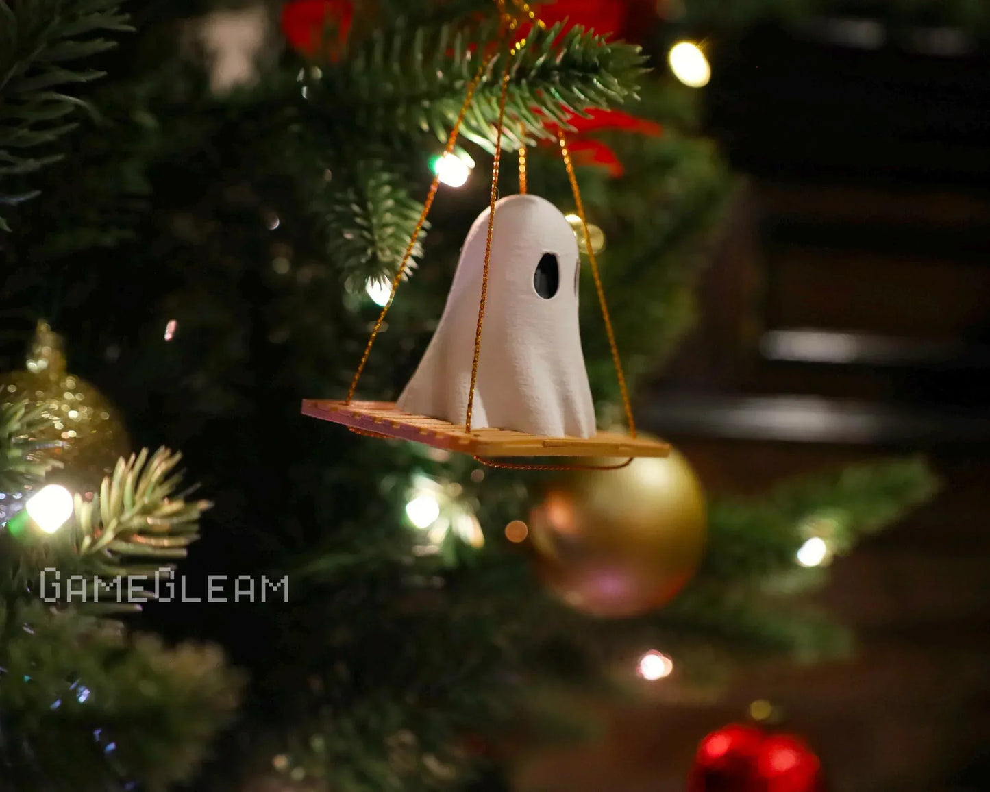 Handmade ghost ornament on a swing hanging from a Christmas tree with festive lights.
