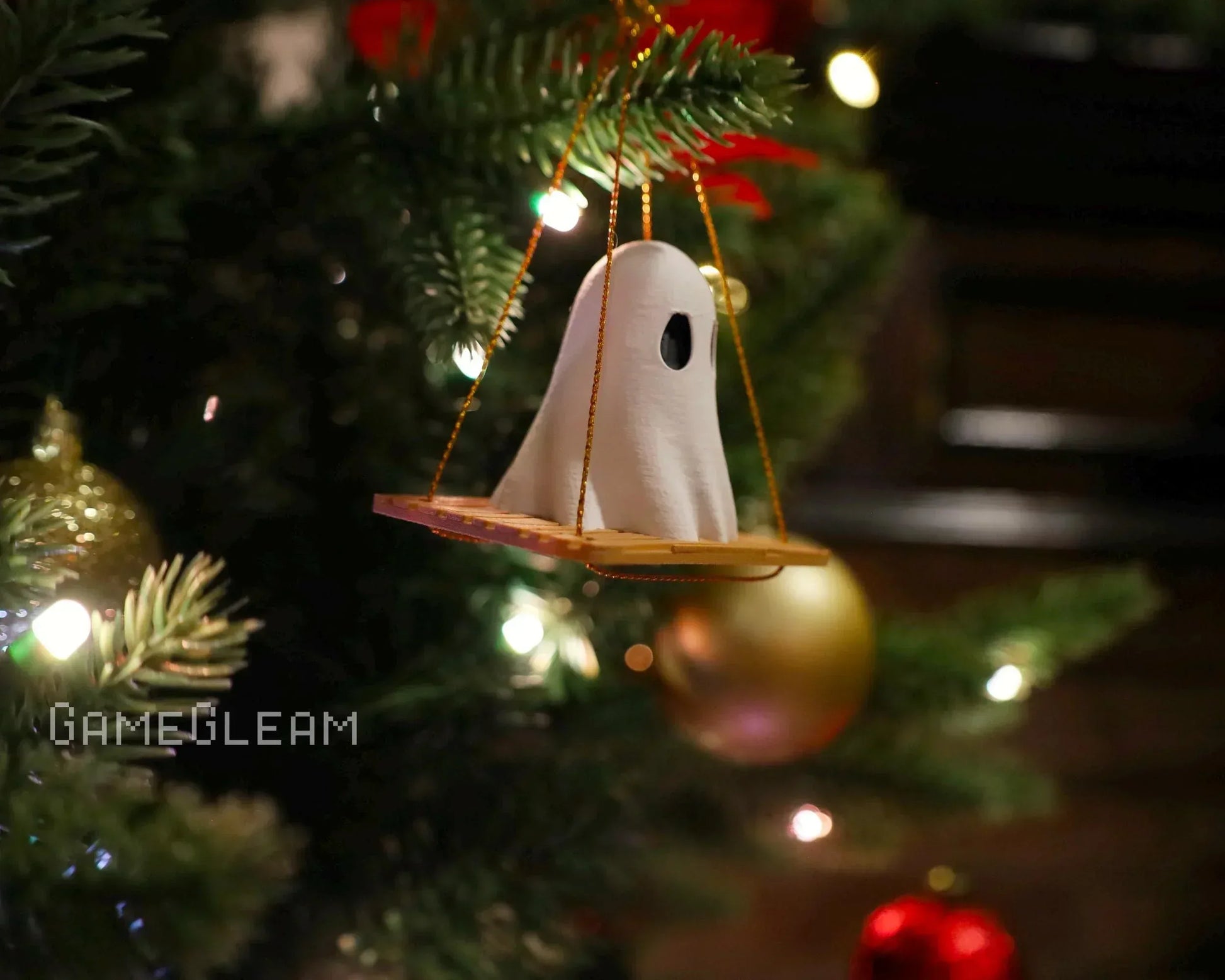 Handmade ghost ornament on a swing hanging from a Christmas tree with festive lights.