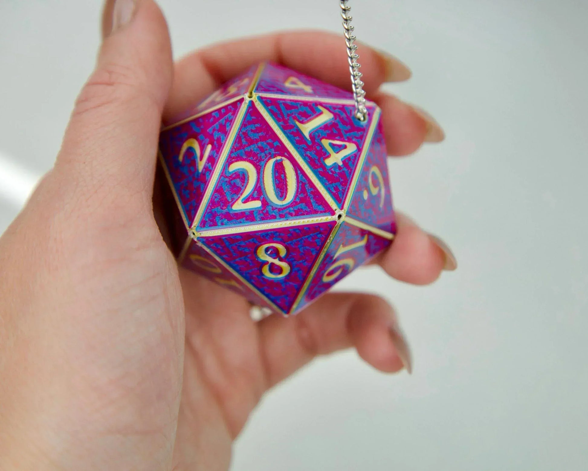 Hand holding a large holographic purple and pink 20-sided dice car charm with gold numbers