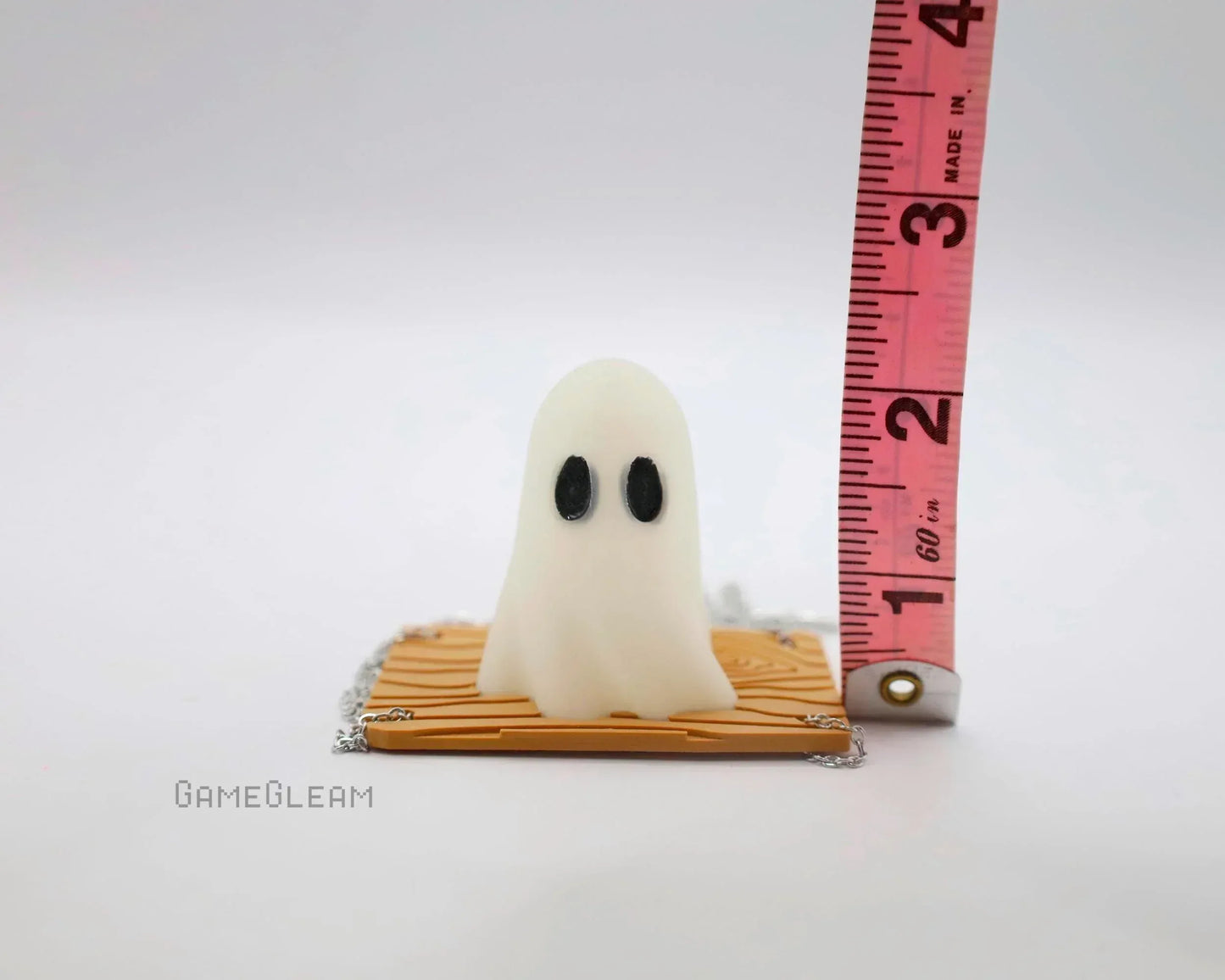 Small handmade ghost figurine with black eyes on a patterned base next to measuring tape