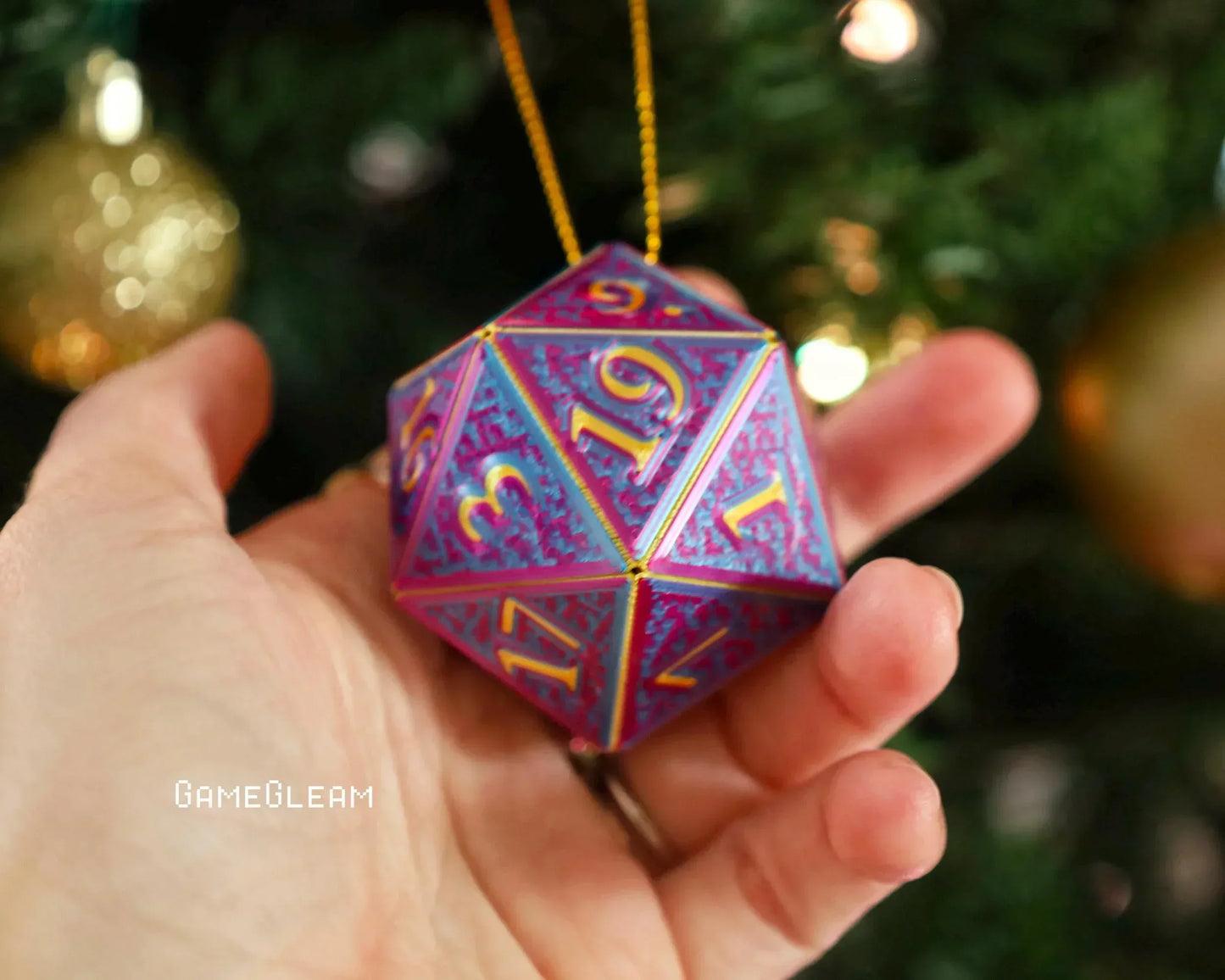 Hand holding a holographic purple and gold 20-sided dice ornament with holiday decor.