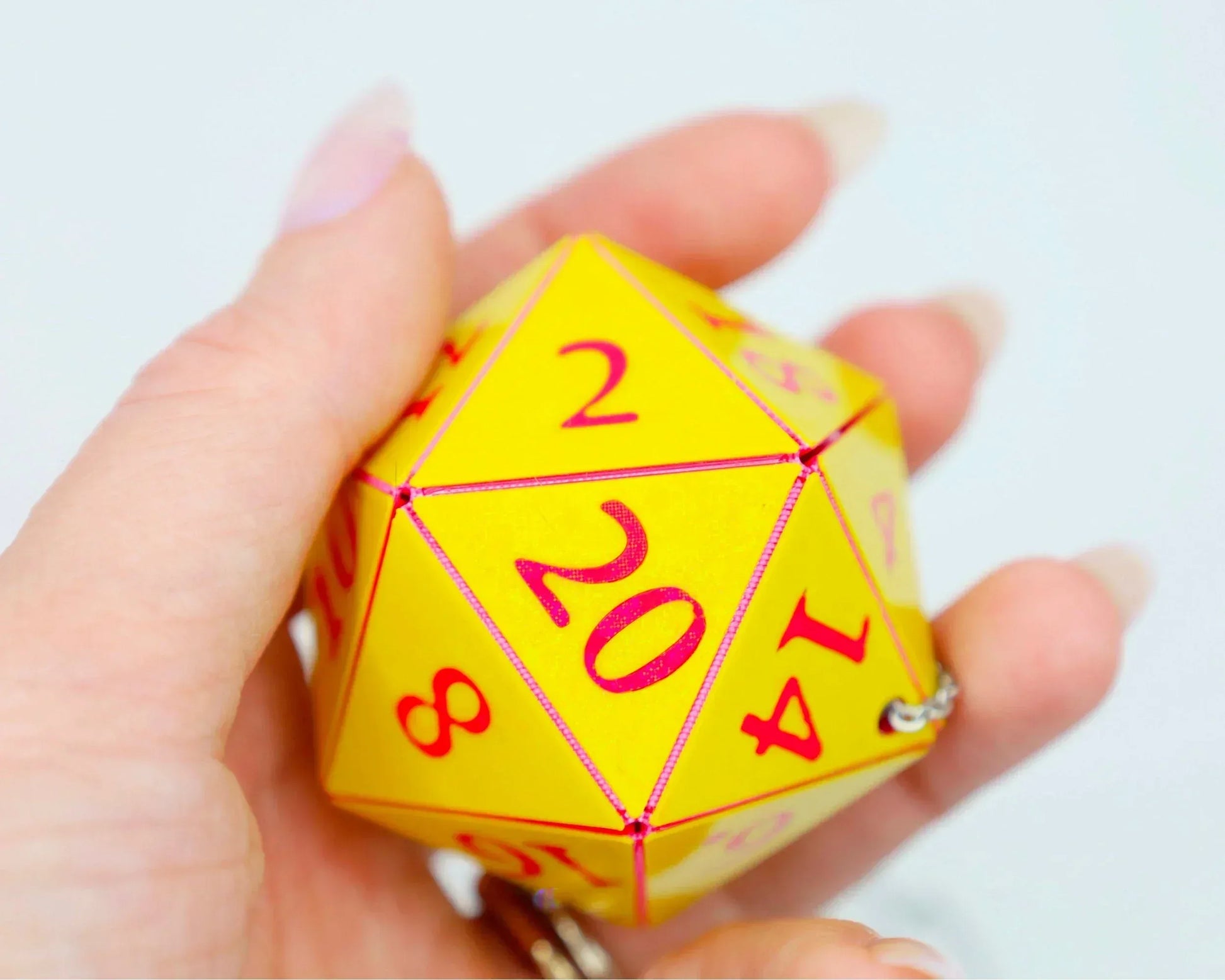 Hand holding a yellow 20-sided polyhedral dice car charm with red numbers