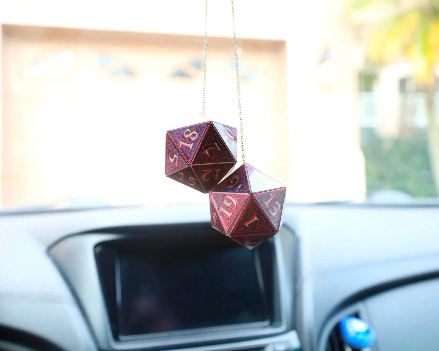 Pair of red twenty-sided dice car charms hanging from rearview mirror in car interior