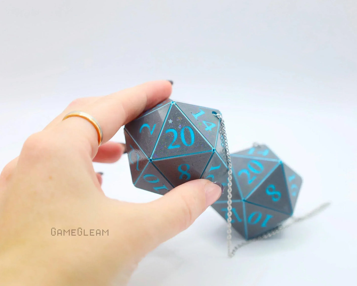 Hand holding large holographic twenty-sided dice charm with blue numbers and chain