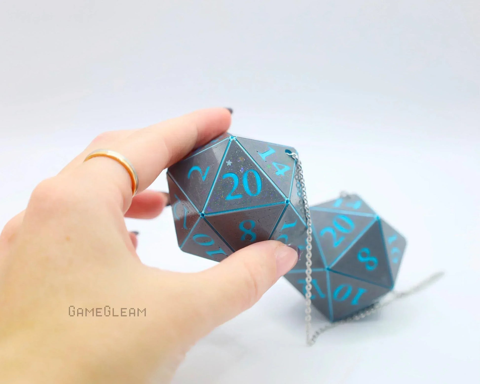 Hand holding large holographic twenty-sided dice charm with blue numbers and chain