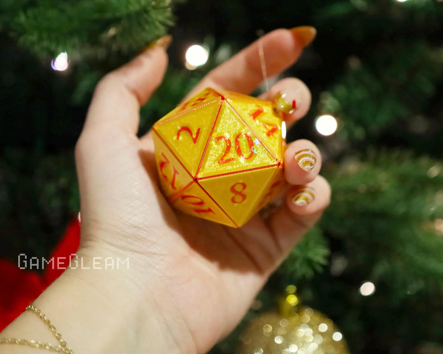 Hand holding a yellow glittery twenty-sided dice ornament by a Christmas tree