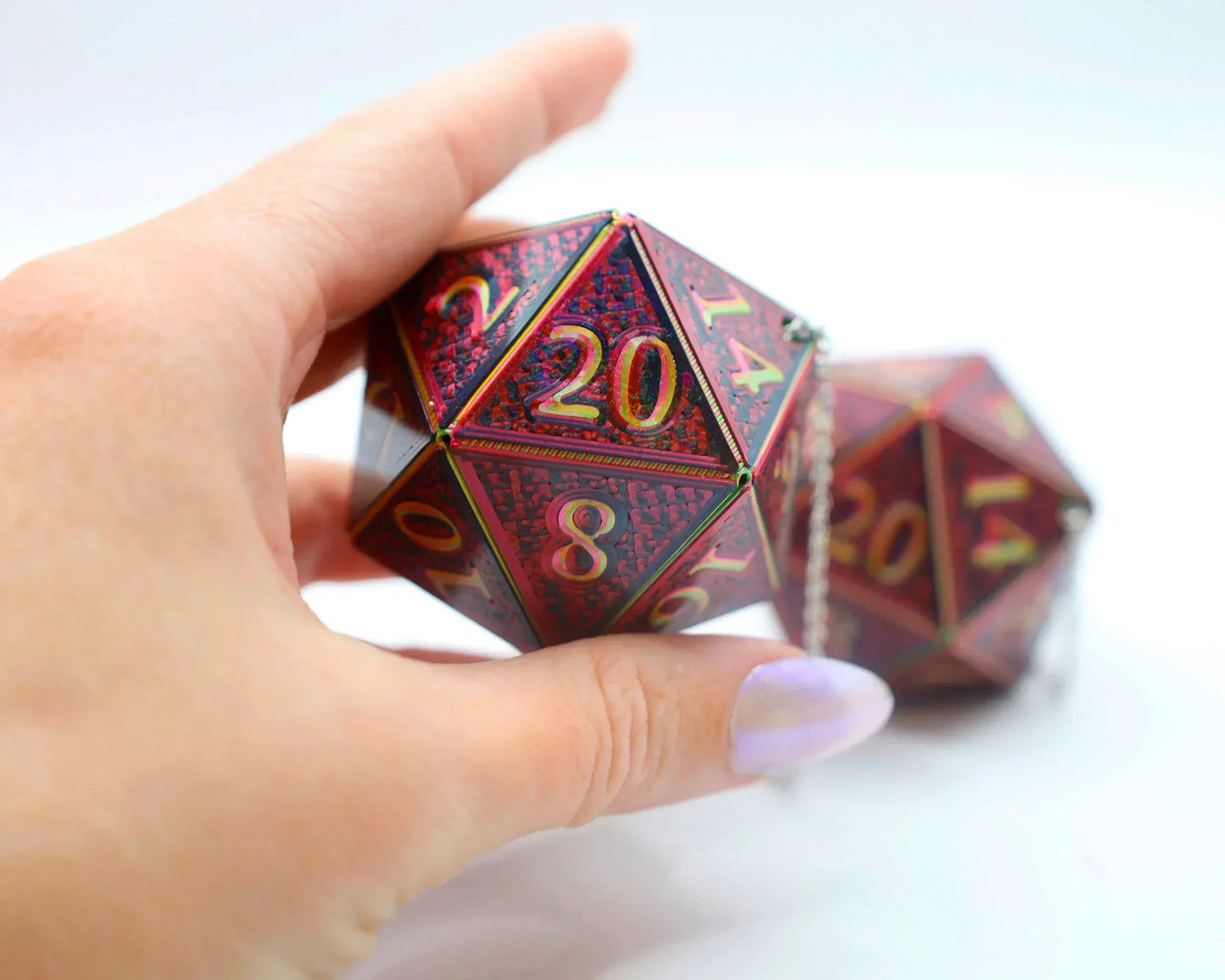 Hand holding a red holographic 20-sided car dice charm with gold numbers on white background
