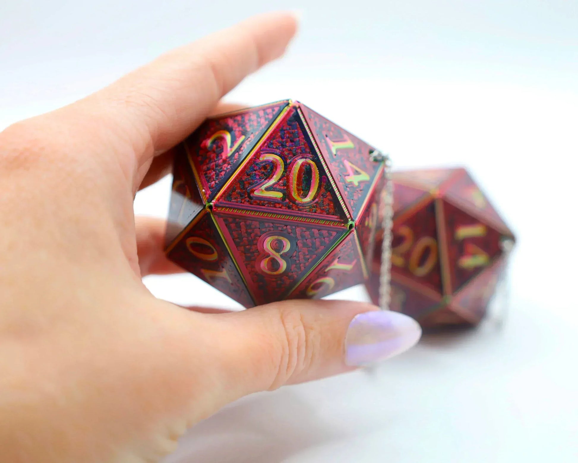Hand holding a red holographic 20-sided car dice charm with gold numbers on white background