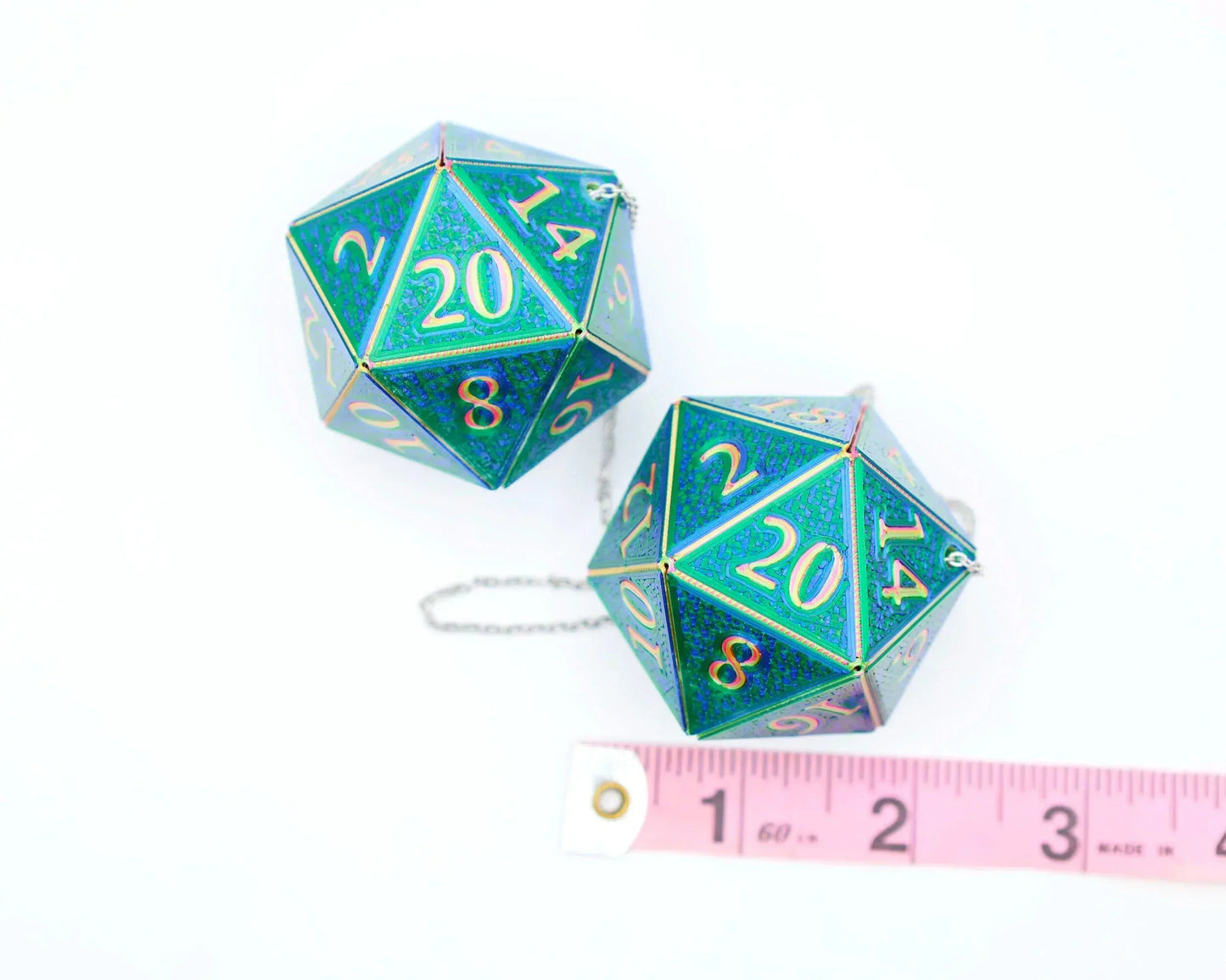 Holographic blue green twenty-sided dice charms with chain, next to pink measuring tape