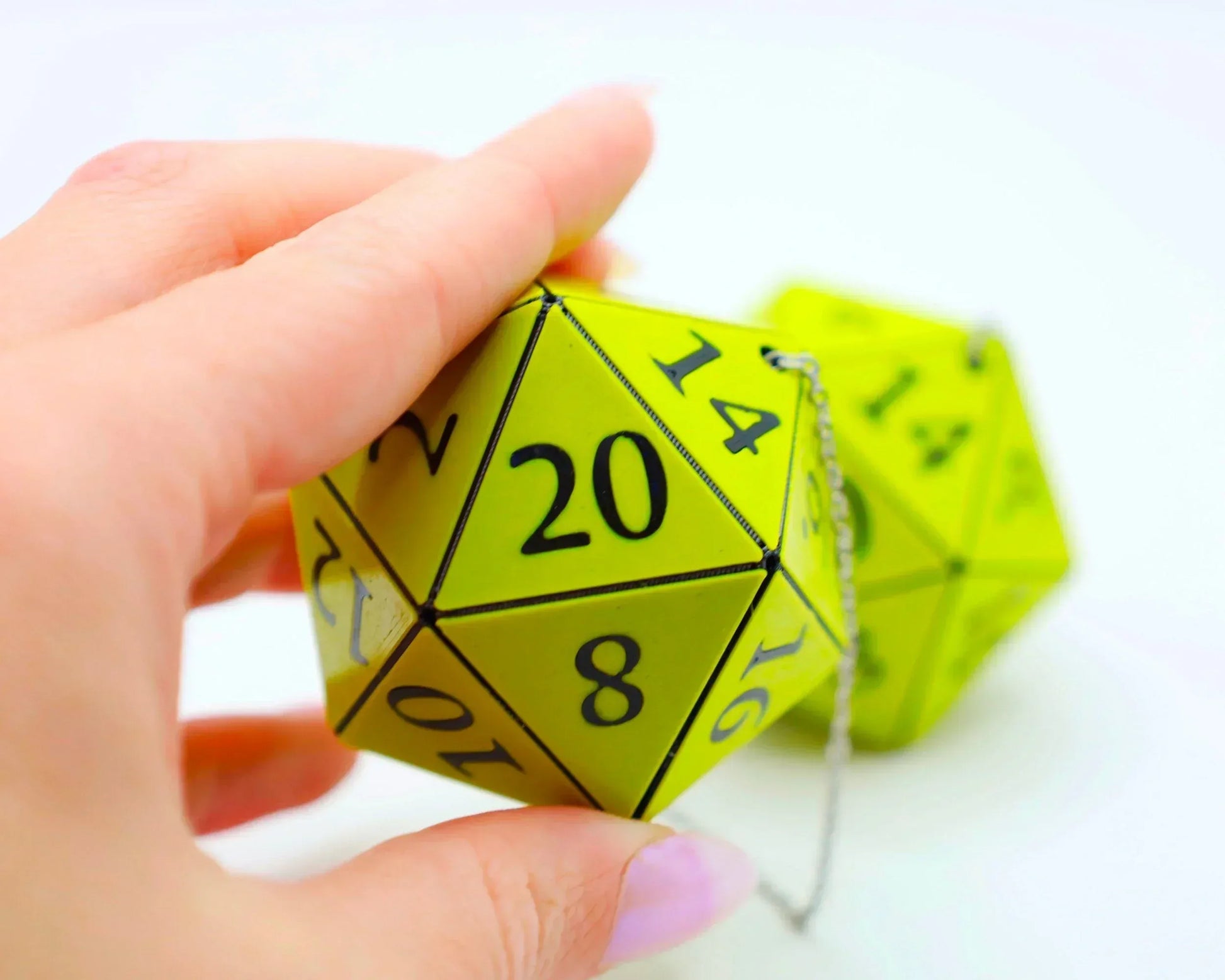 Hand holding a bright green twenty-sided dice car charm with numbers and a metal chain