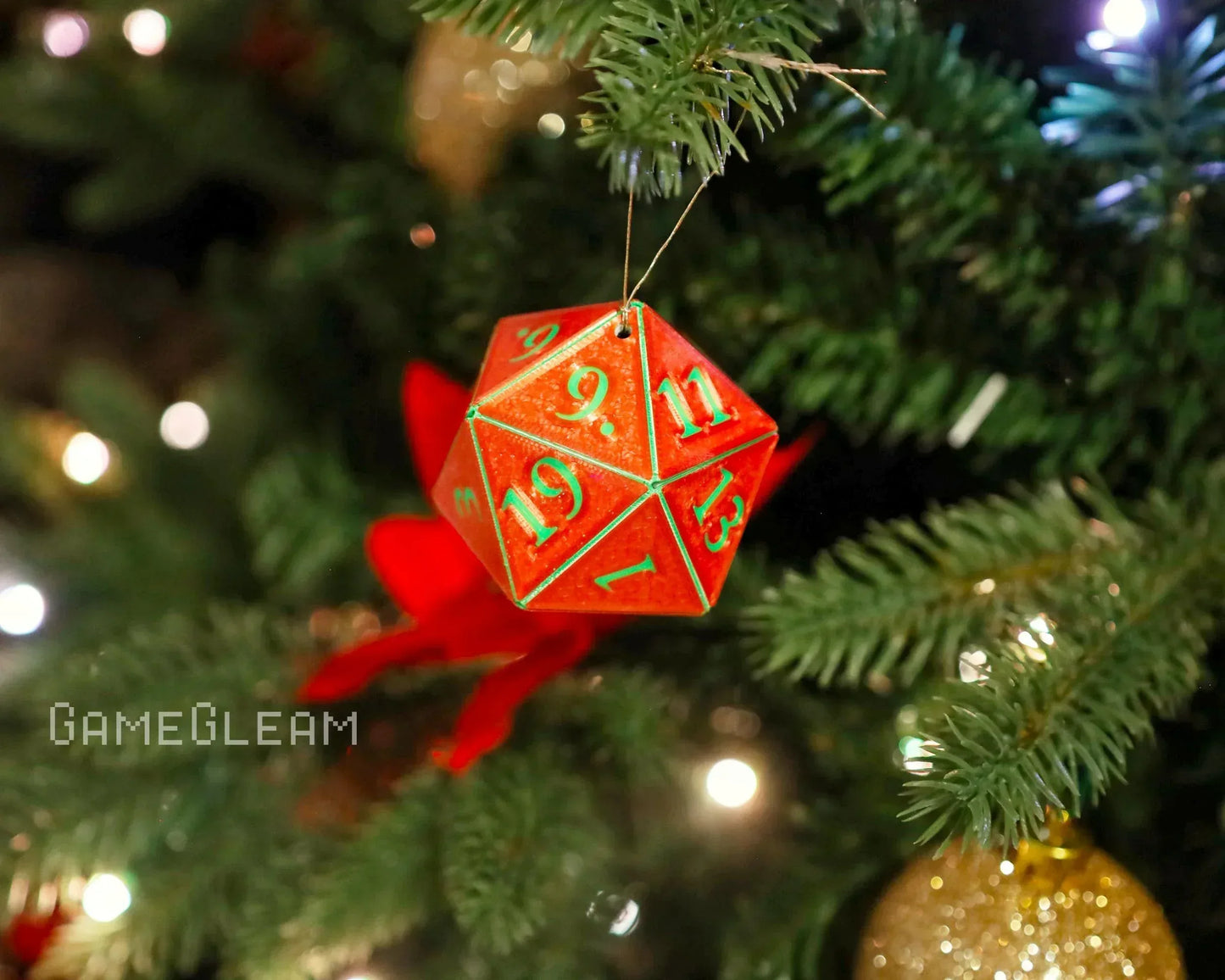 Handmade red twenty-sided dice ornament with green numbers hanging on a Christmas tree