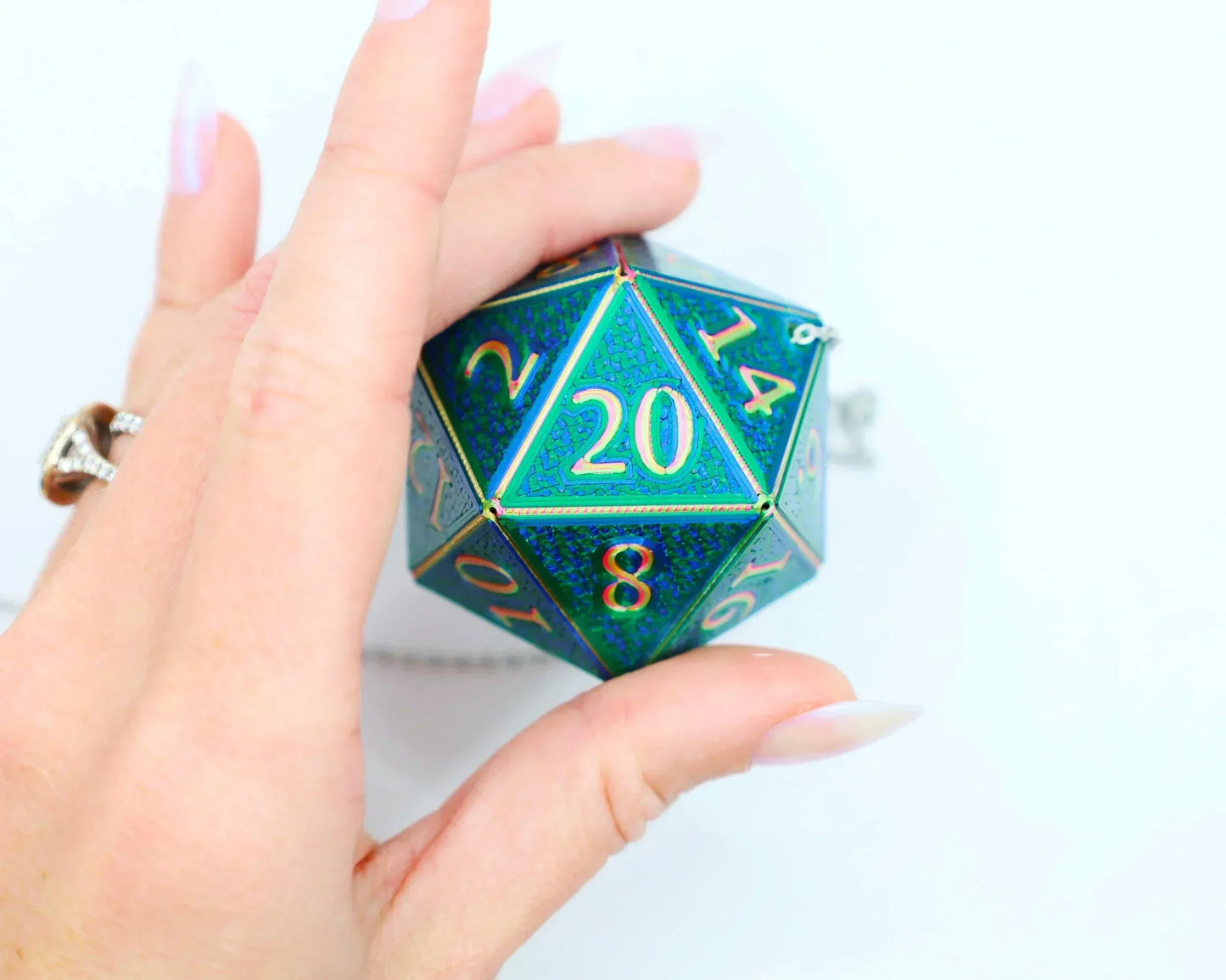 Hand holding holographic green blue D20 dice charm with gold numbers for gamers