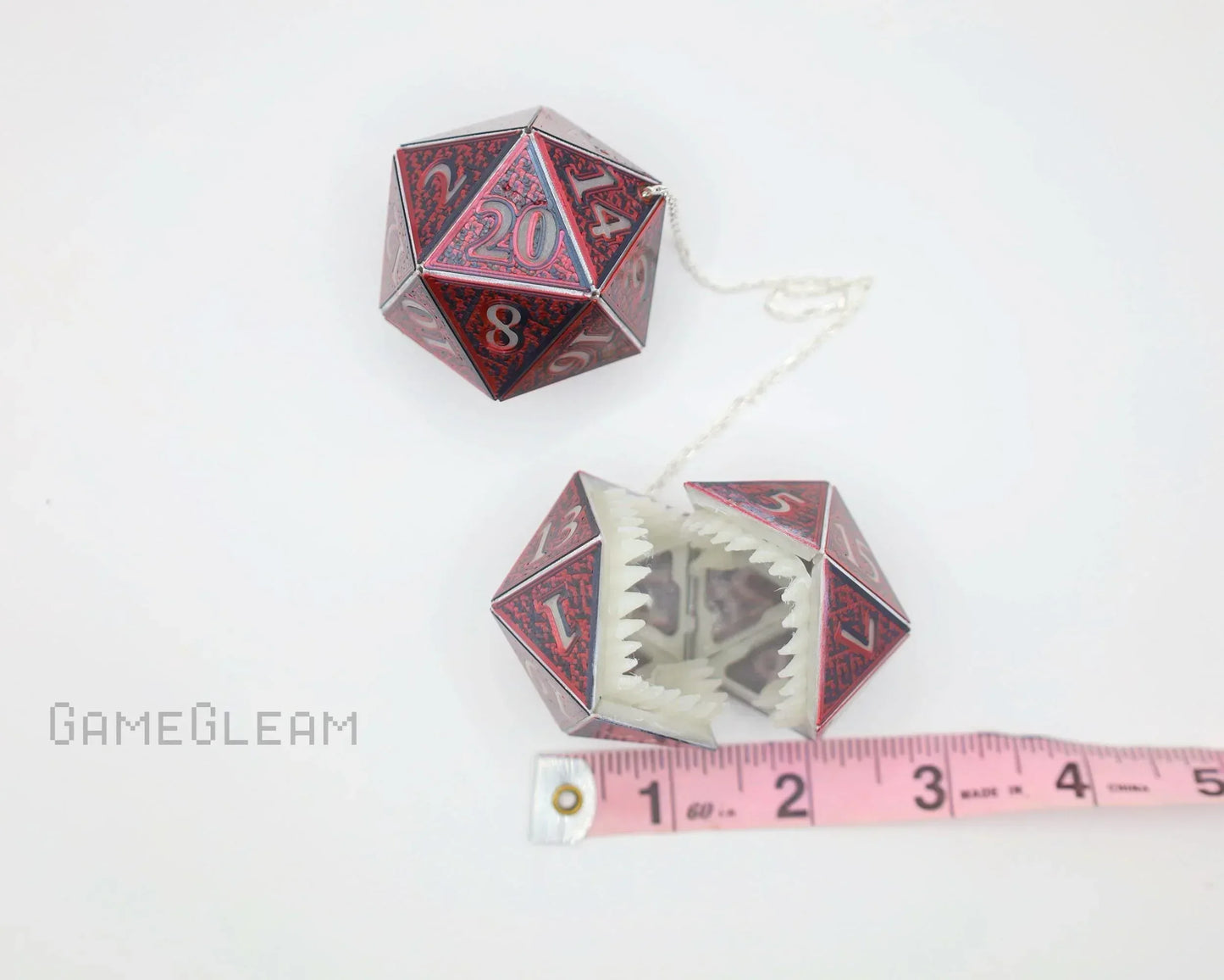 Handmade red and black twenty-sided dice car charm with monster teeth, shown with measuring tape
