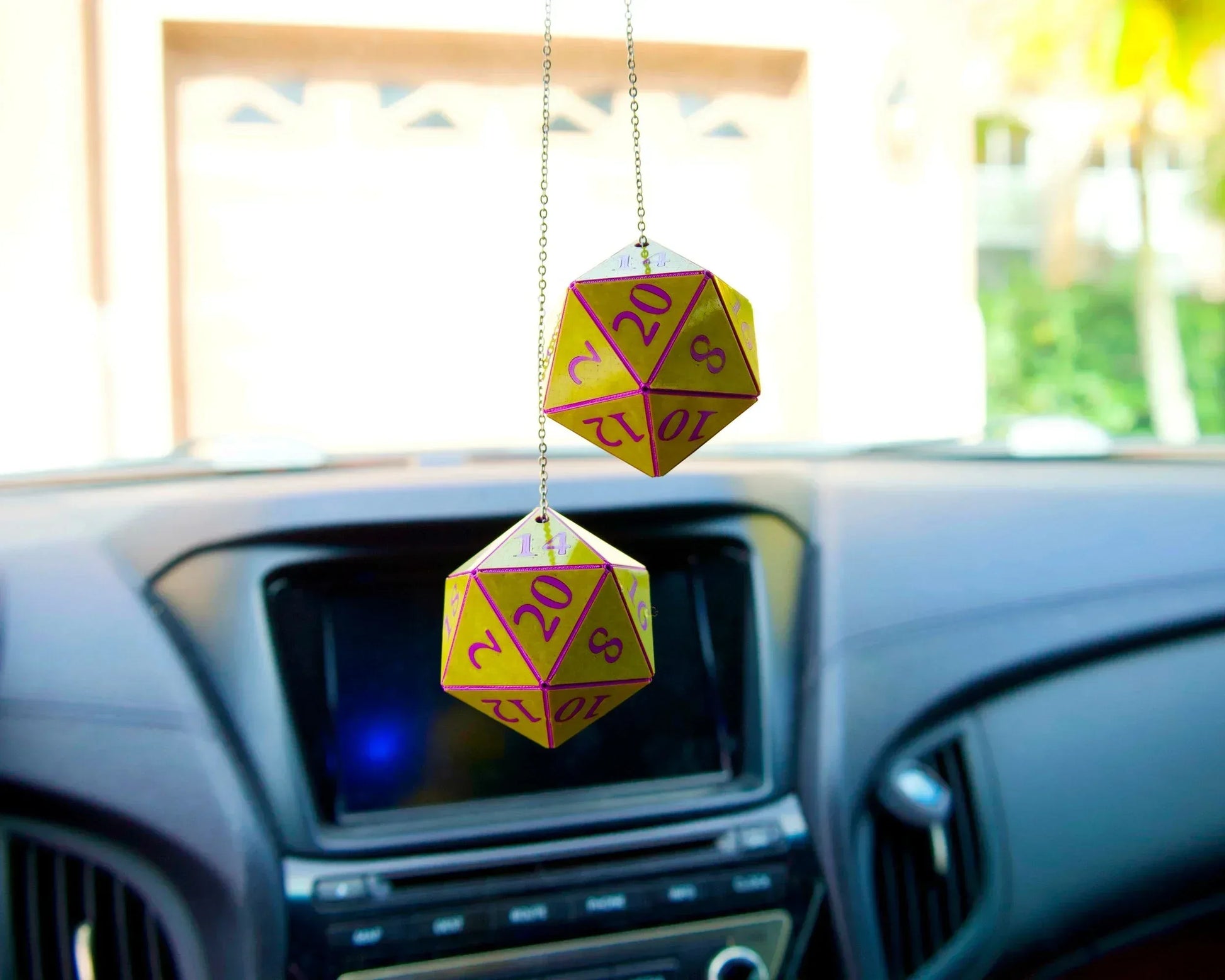 Yellow and purple twenty-sided dice car charms hanging from rearview mirror in vehicle interior