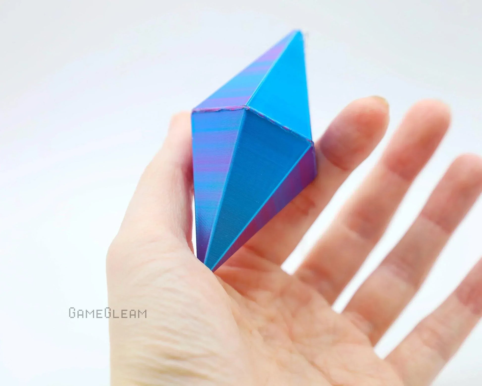 Hand holding a blue and purple geometric polyhedral dice charm against a white background