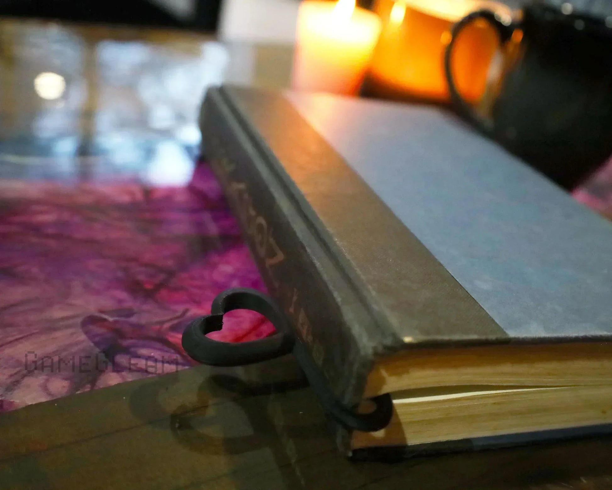 Heart-shaped black book holder on a closed book, candle and mug in background, cozy setting