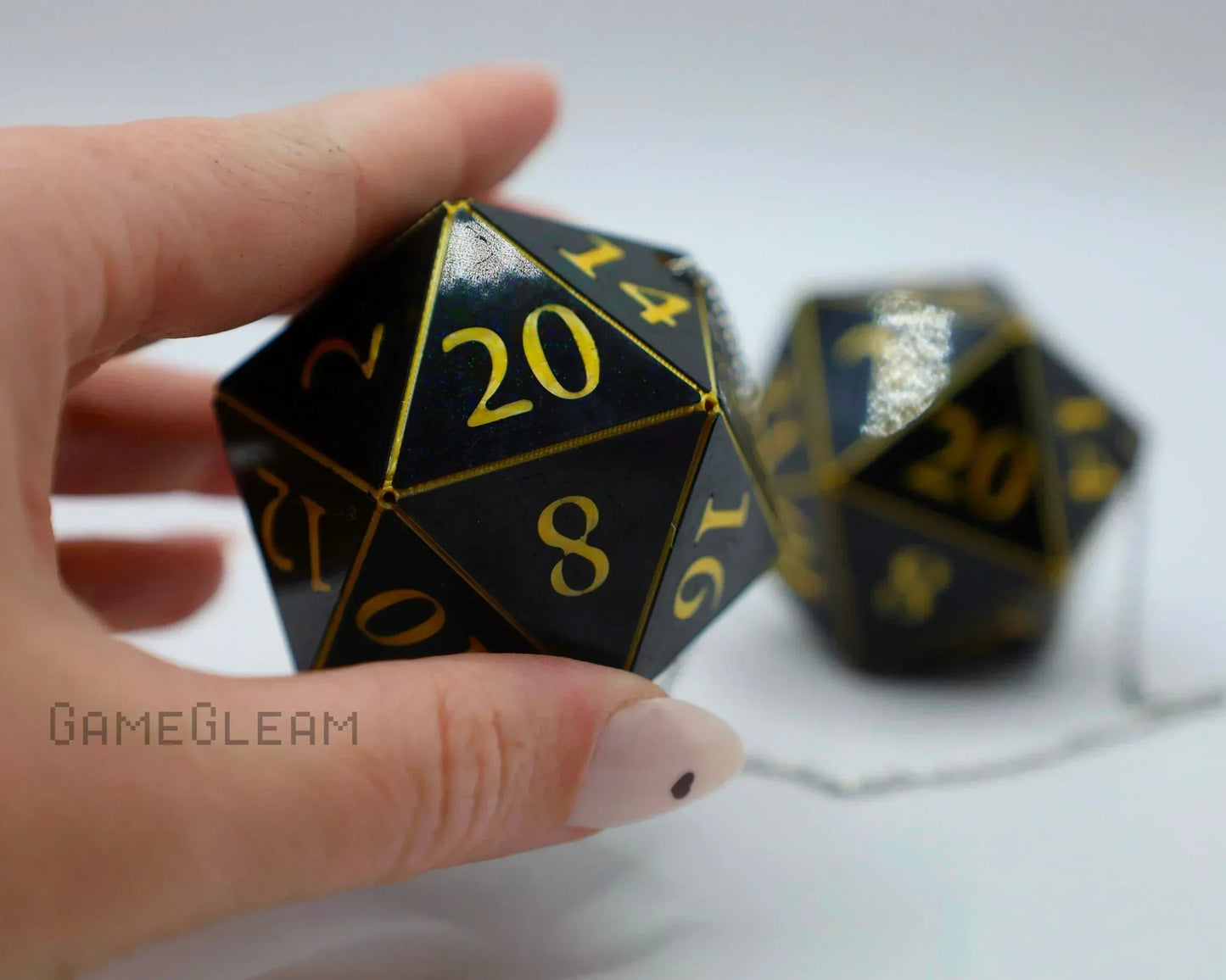 Hand holding black 20-sided dice charm with gold numbers, shown with chain for car accessory.