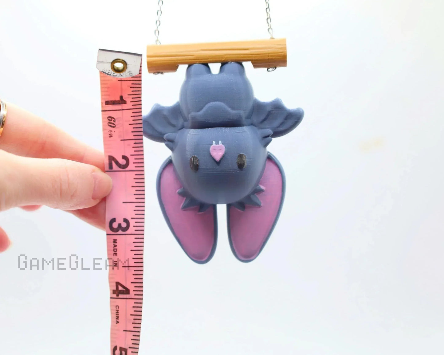 Cute purple bat car charm with pink wings hanging from a wood rod, measured by tape.