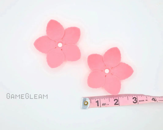 Two pink five-petal flower-shaped charms with a central hole, next to a measuring tape