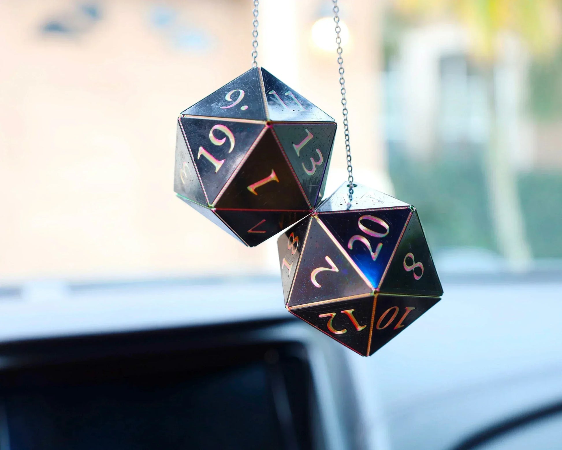 Holographic twenty-sided dice car charms hanging on a chain in a vehicle interior.