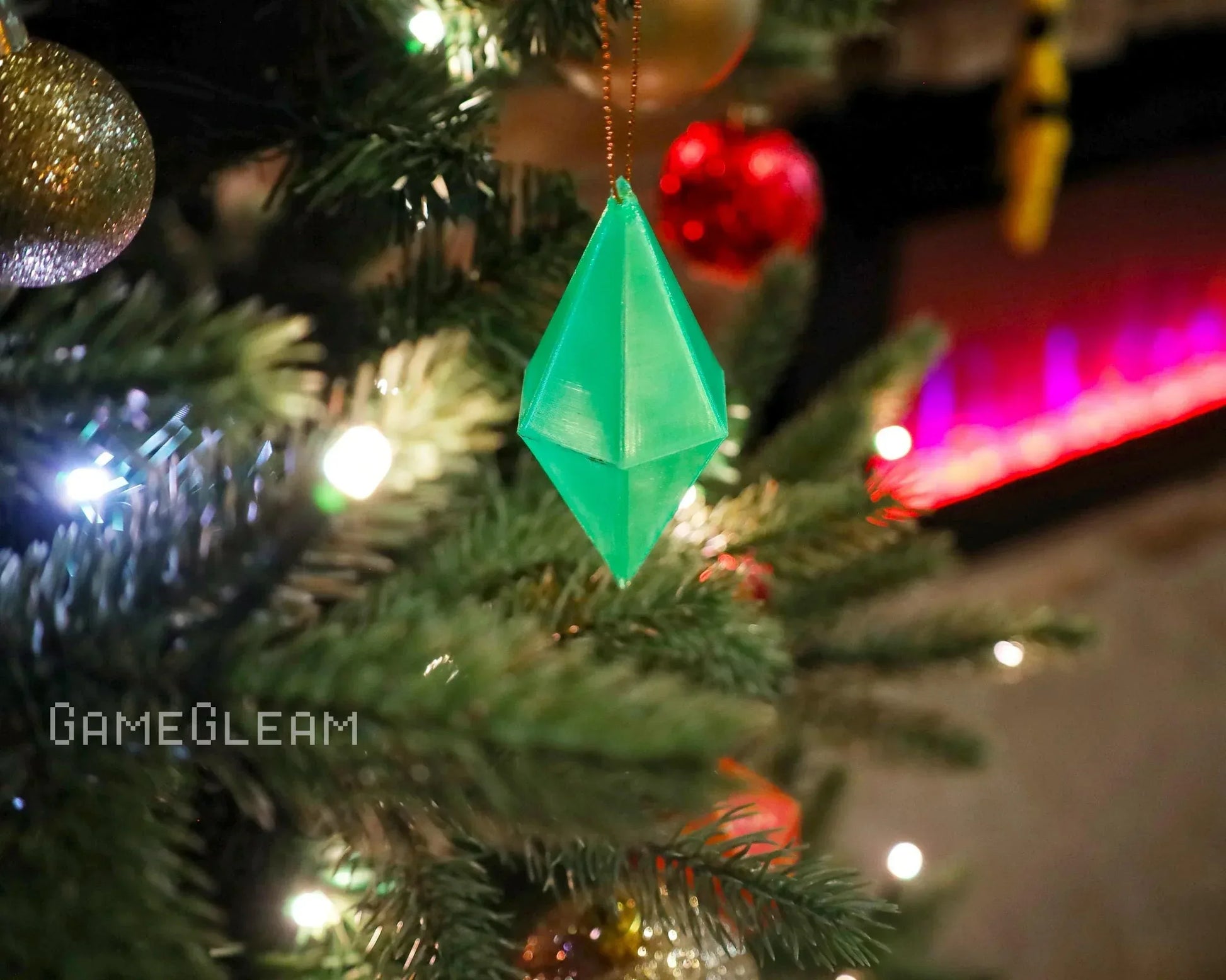 Green geometric gamer ornament hanging on a Christmas tree with festive lights
