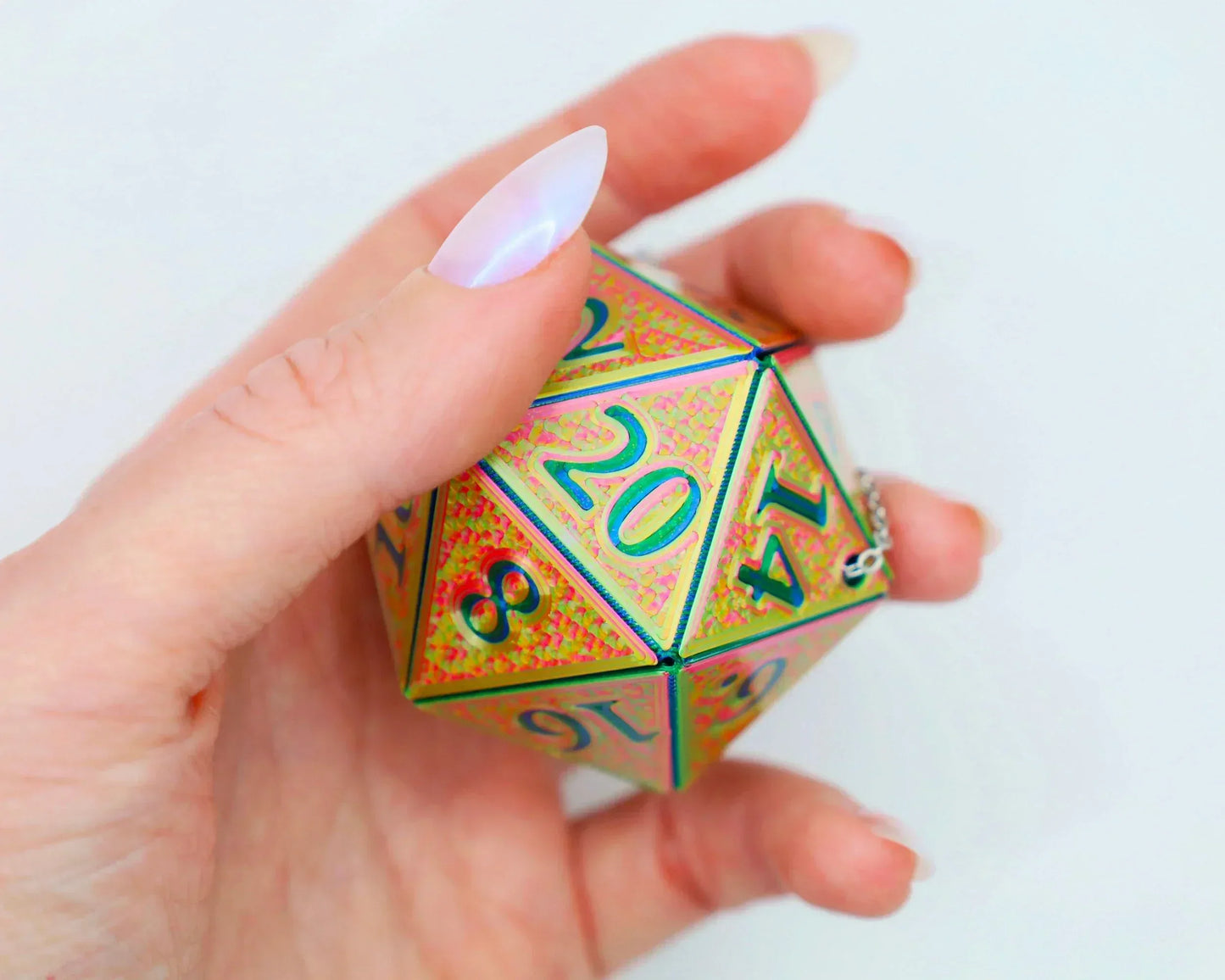 Hand holding a holographic 20-sided dice charm with metallic green and pink finish